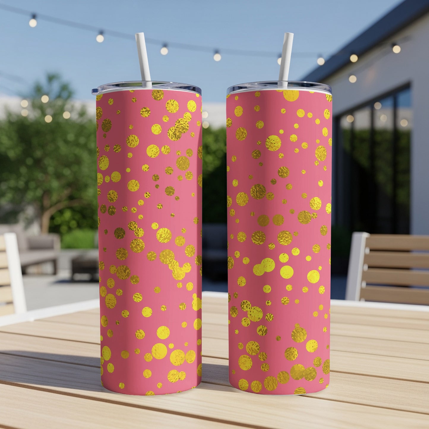 Two pink tumblers with gold polka dots and straws sit on a wooden table.