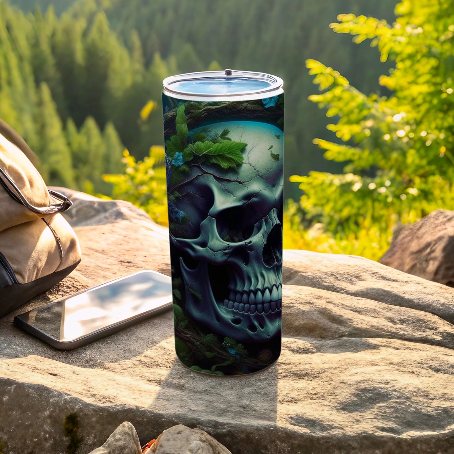 Dark skull tumbler adorned with blue flowers, set on rocks with a forest background.