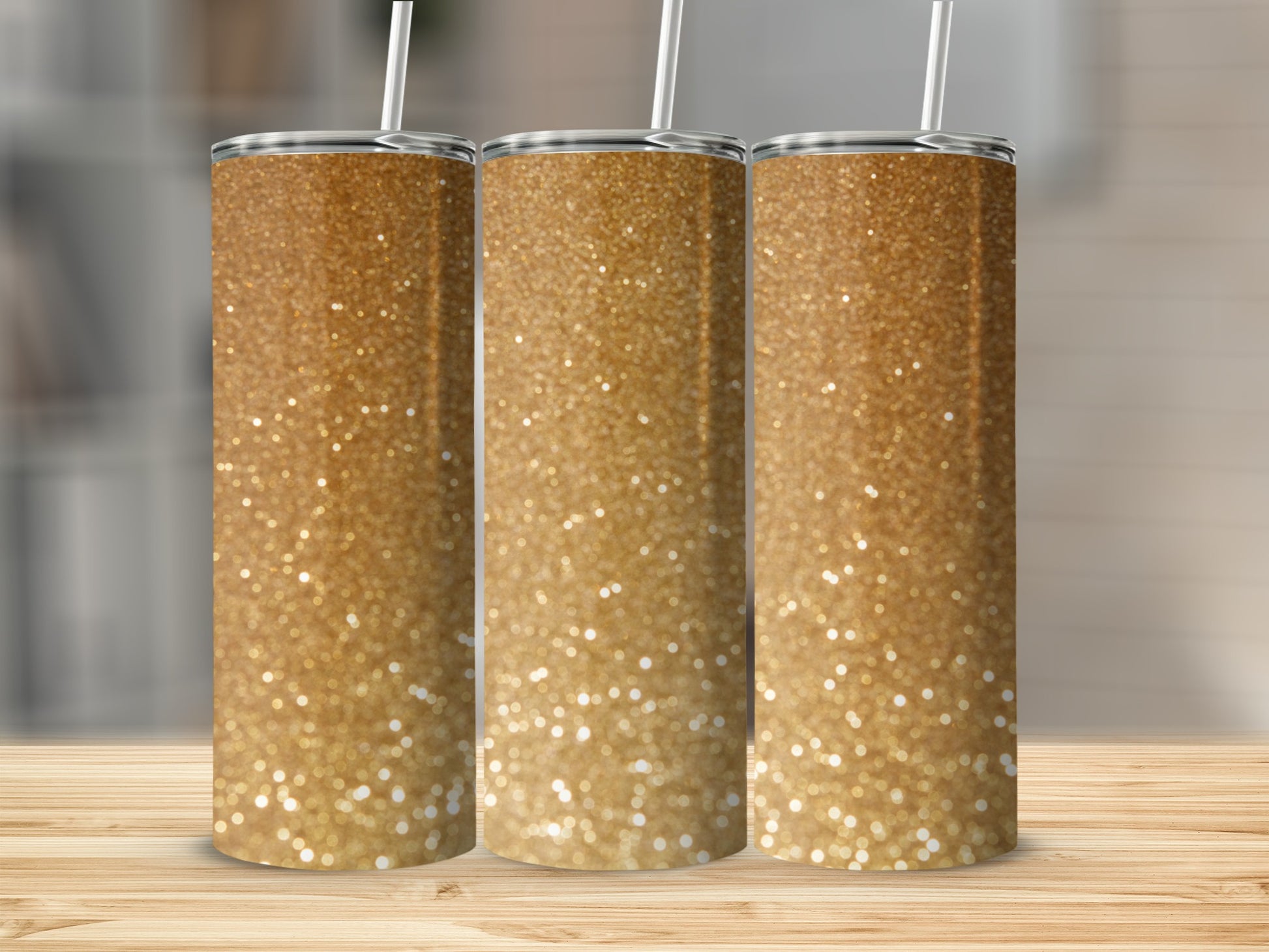Three glittery gold tumblers with straws on a wooden surface.