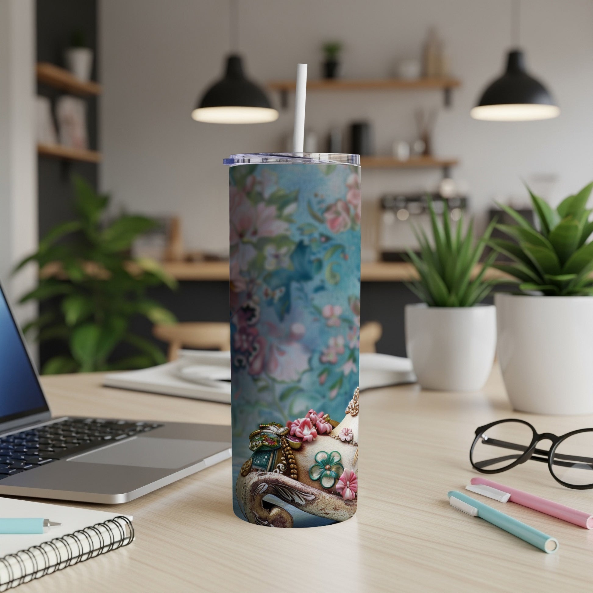 Floral skinny tumbler with a straw, on a desk with a laptop and pens.