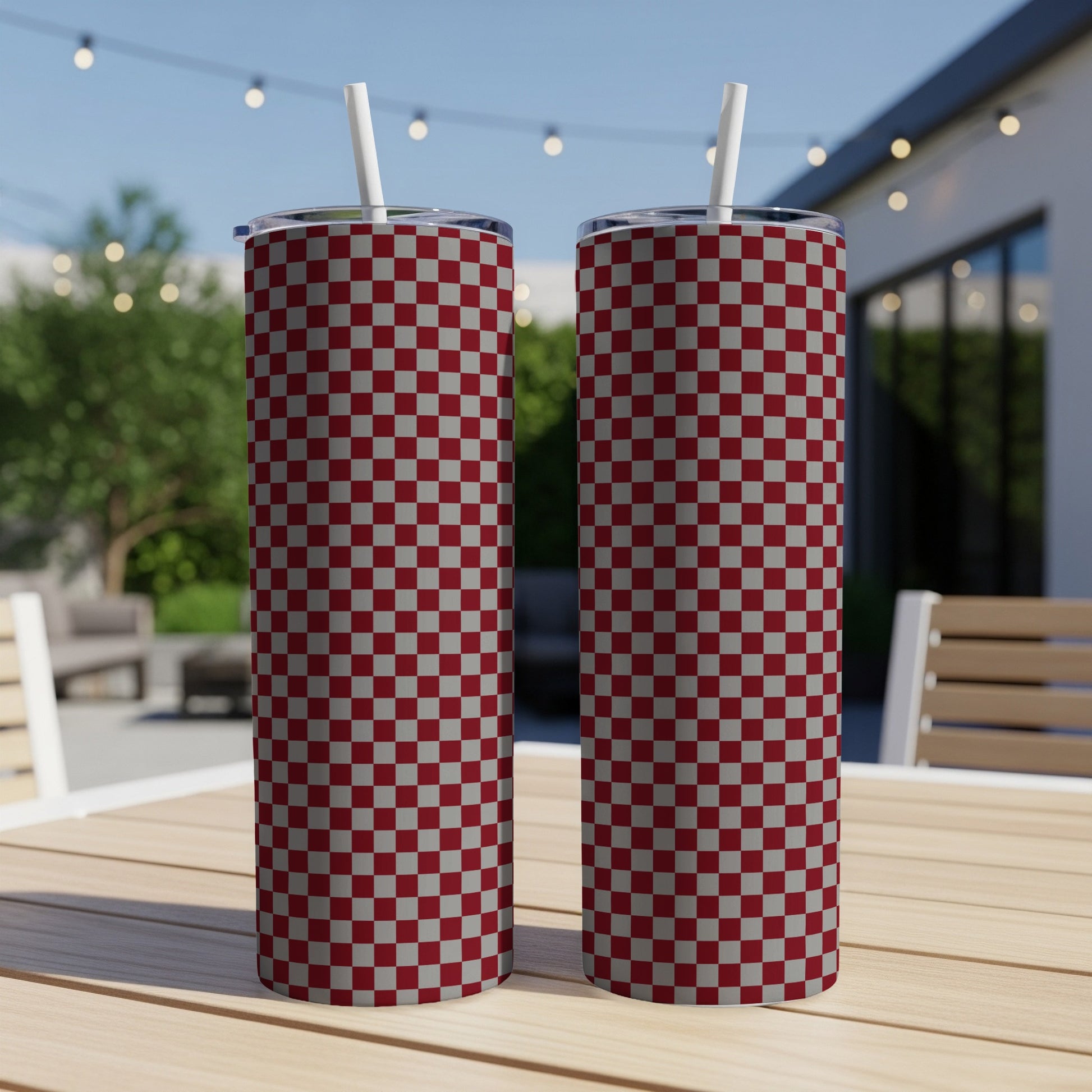 Two maroon and grey checkered tumblers with straws on a wooden table.