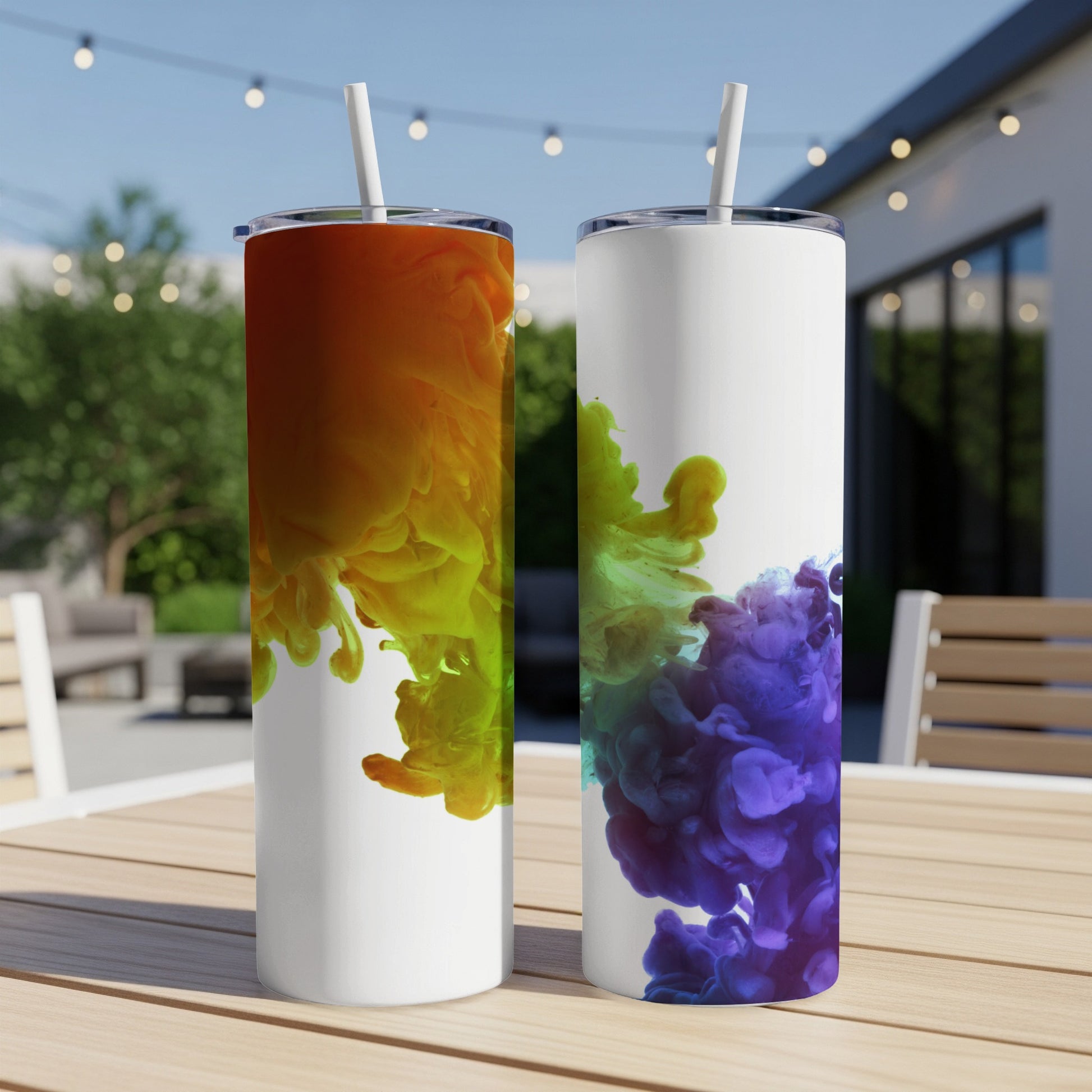 Two tumblers with colorful ink splashes on a wooden table outdoors.