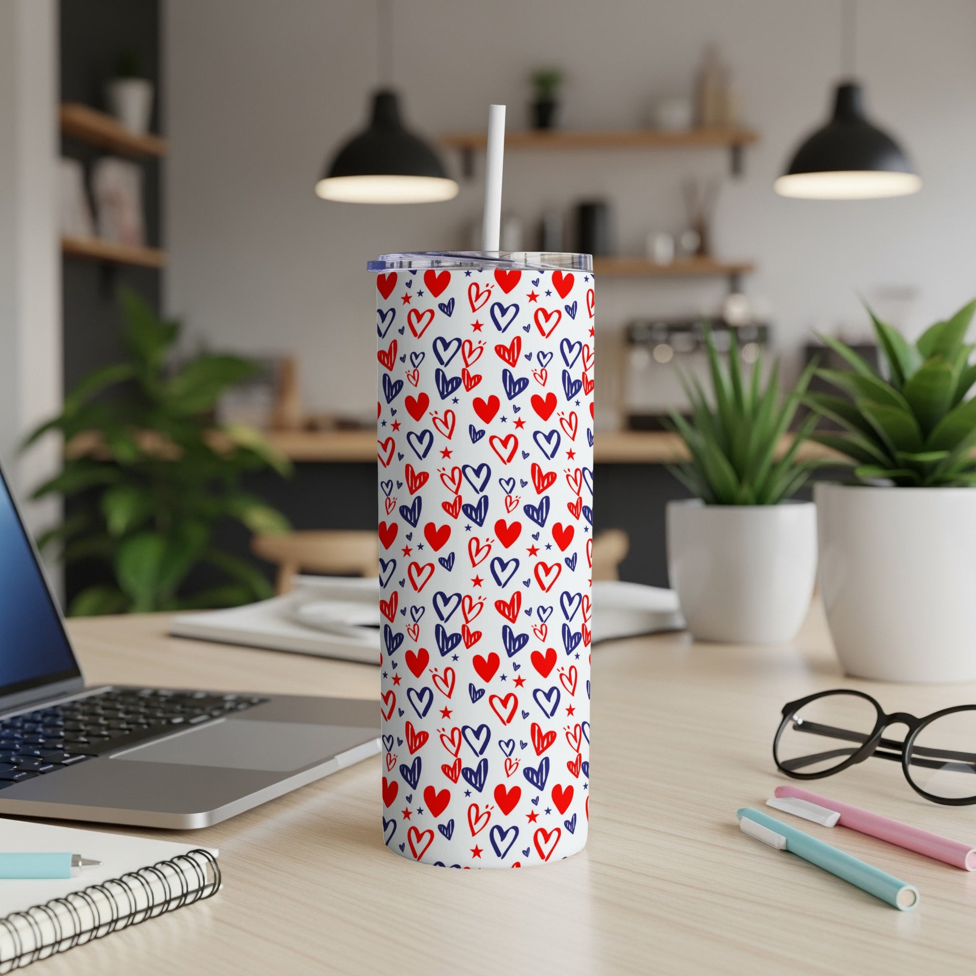 White skinny tumbler with red and blue hearts pattern, straw in lid.