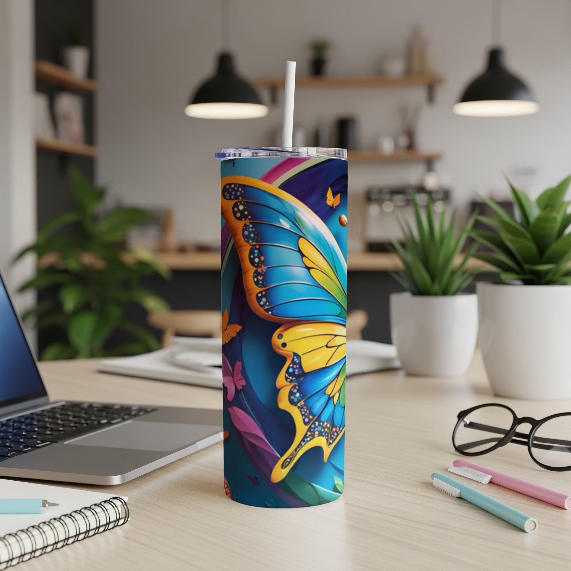 Tall tumbler with blue and yellow butterfly design and straw, on a desk.