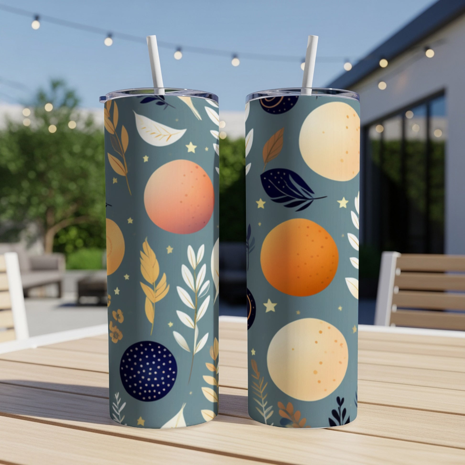 Two tumblers with celestial moon and leaf pattern on outdoor table.