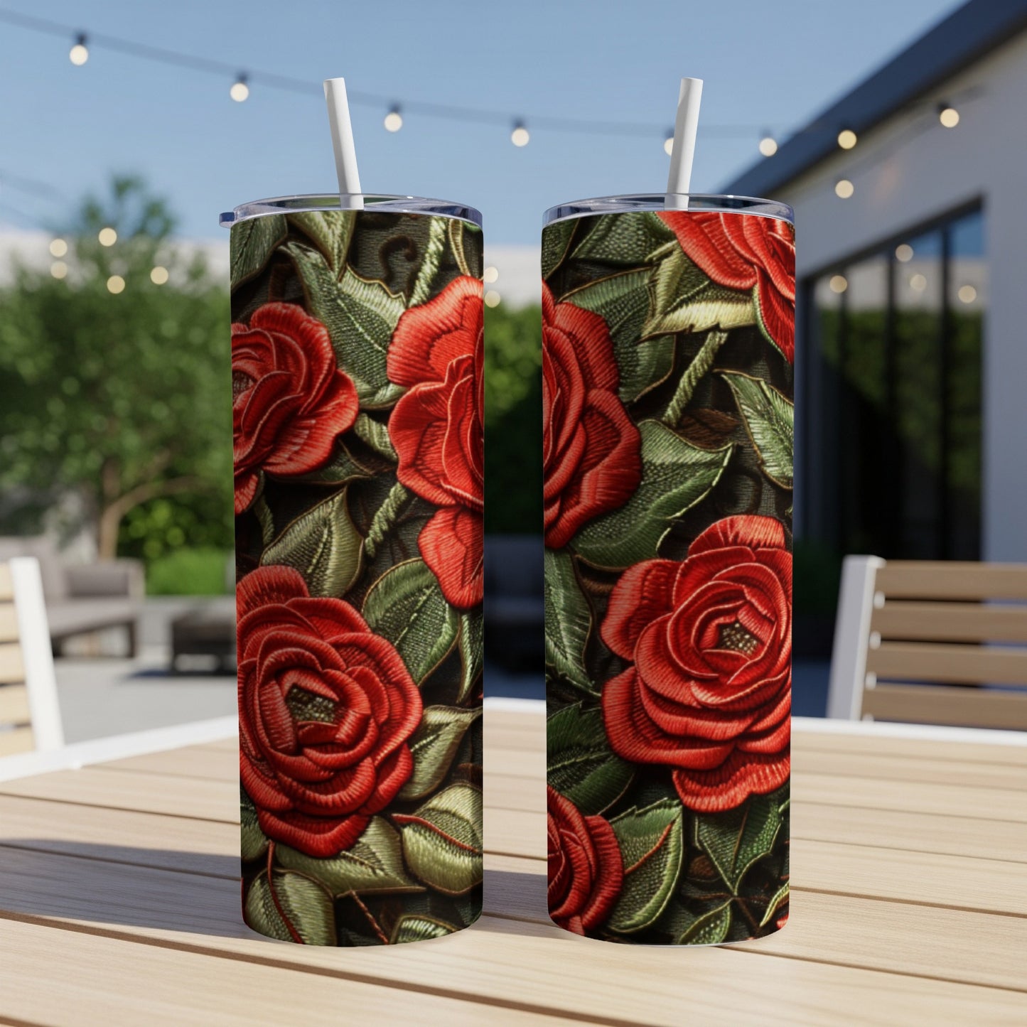 Two tumblers with a red rose embroidered pattern on a wooden table outdoors.