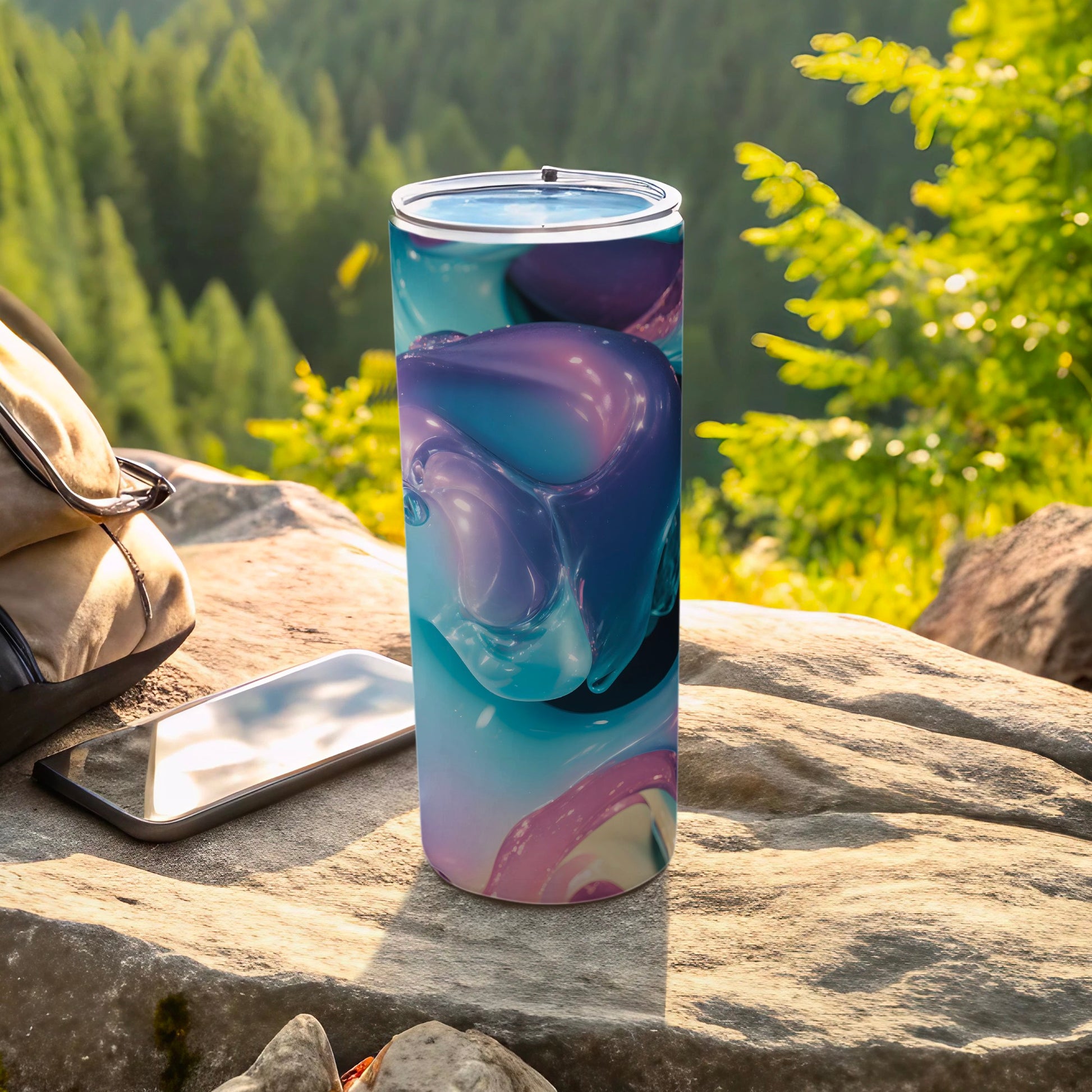 Abstract fluid art tumbler with a phone and backpack on a rock.