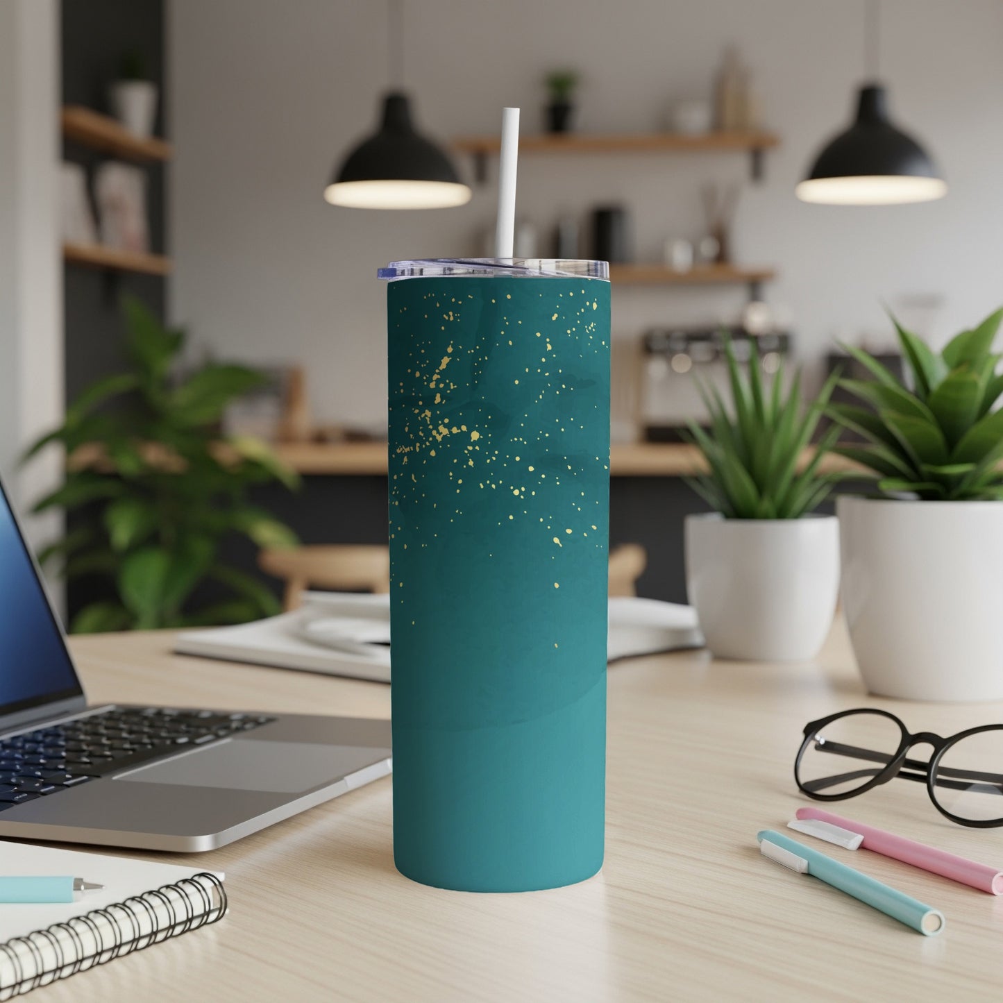 Teal tumbler with gold splatter pattern and straw, on a desk.