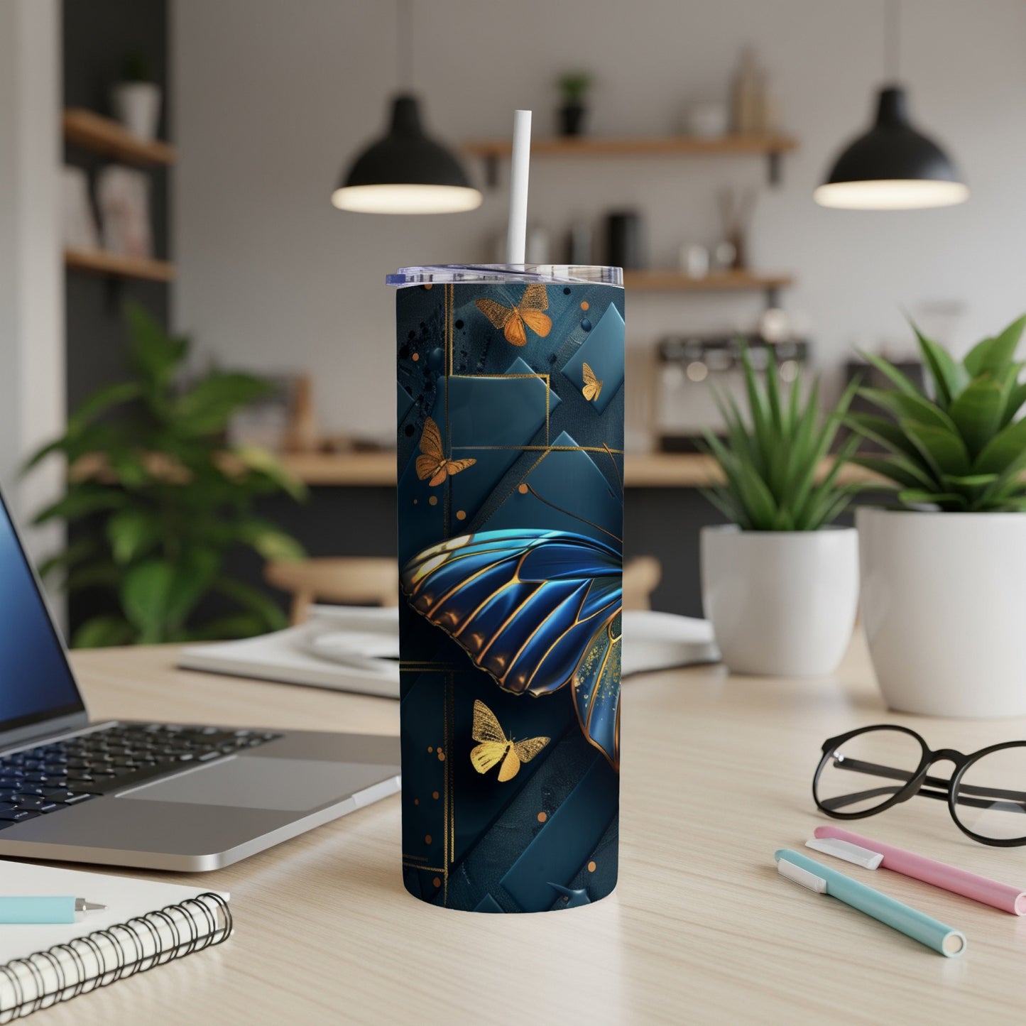 Tall tumbler with blue and gold butterfly design, straw, on a desk.