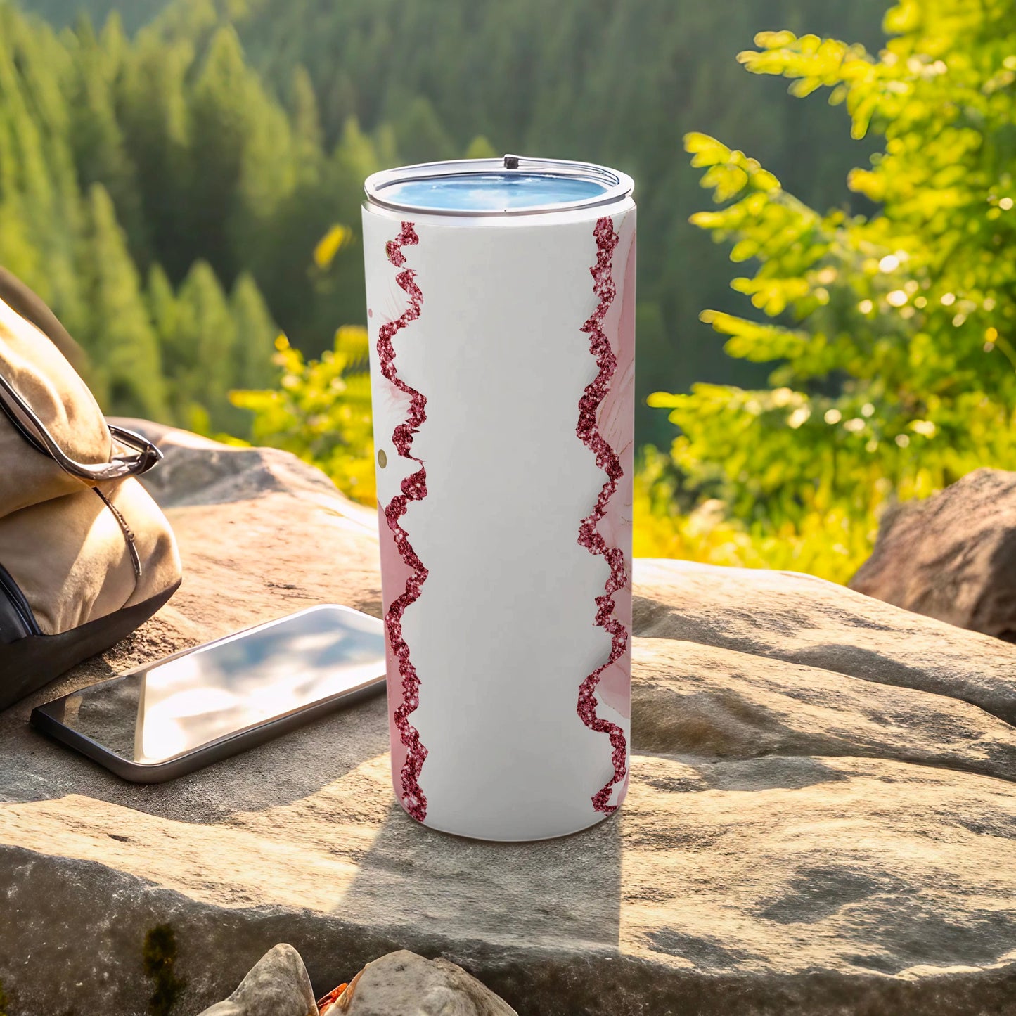 White tumbler with pink floral design and glitter accents, next to a phone and backpack.