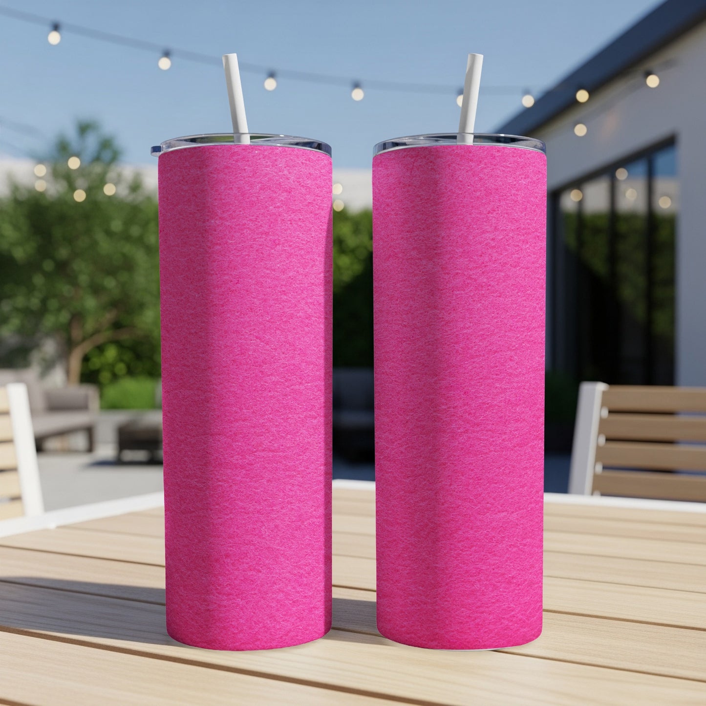 Two pink tumblers with white straws sit on a wooden table outdoors.