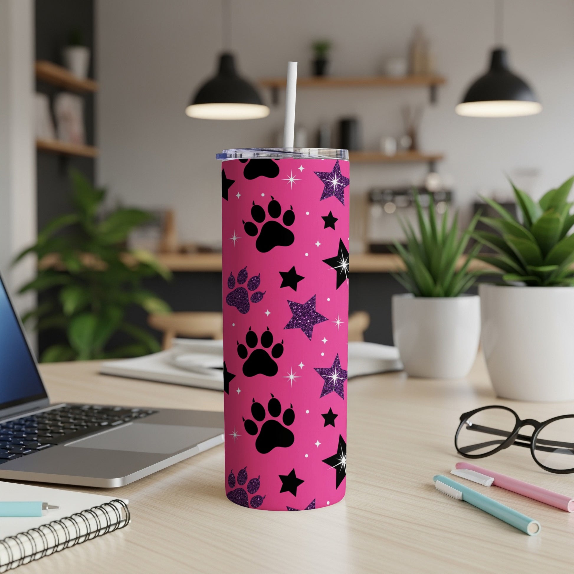 Pink tumbler with black paw prints and glitter stars, on a desk.