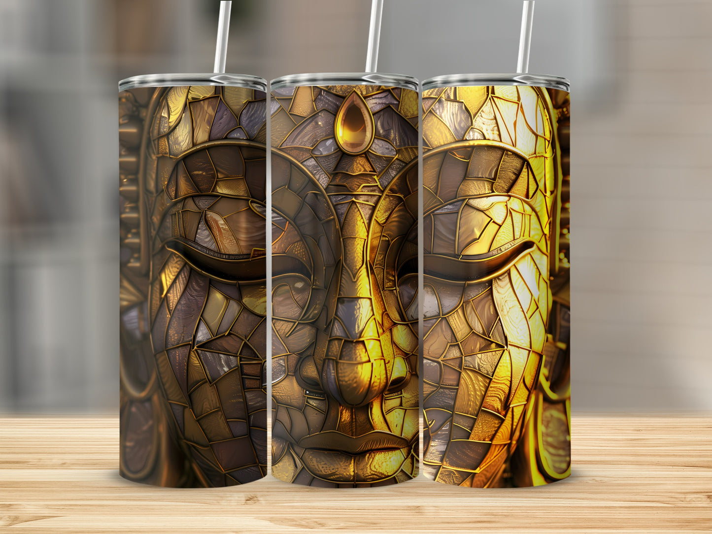 Three tumblers with intricate golden Buddha face design on a wooden surface.