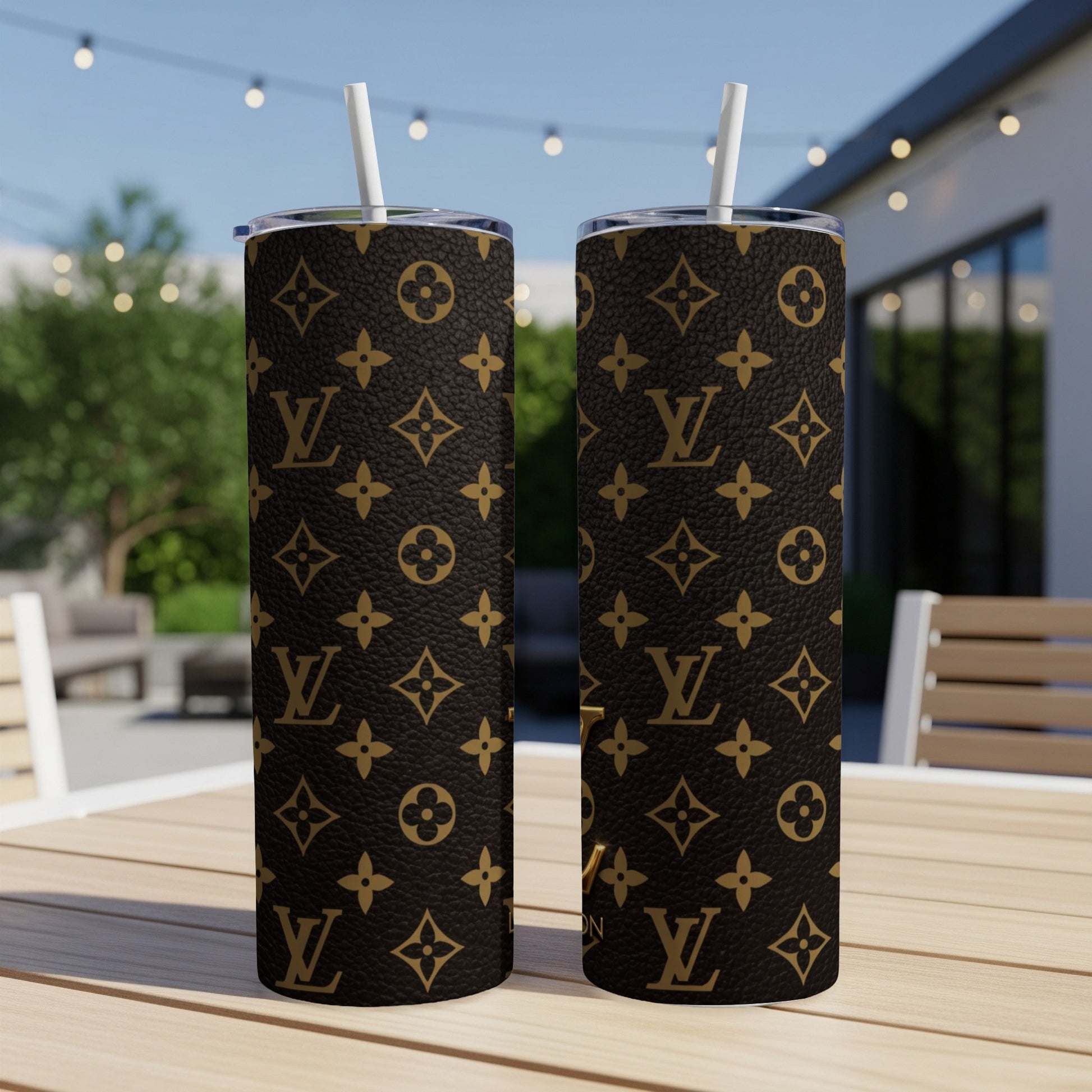 Two tumblers with a classic monogram pattern and straws are on a wooden table outdoors.