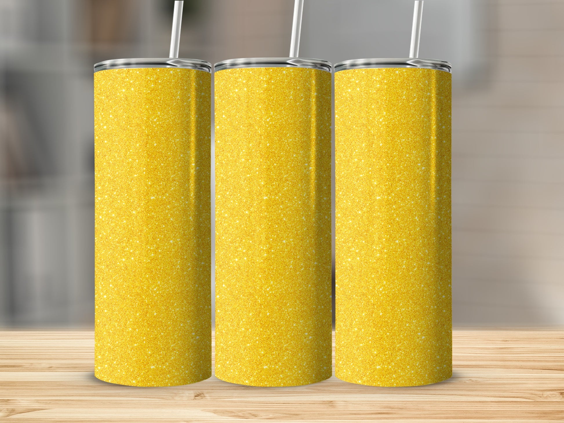 Three glittery gold tumblers with white straws on a wooden surface.