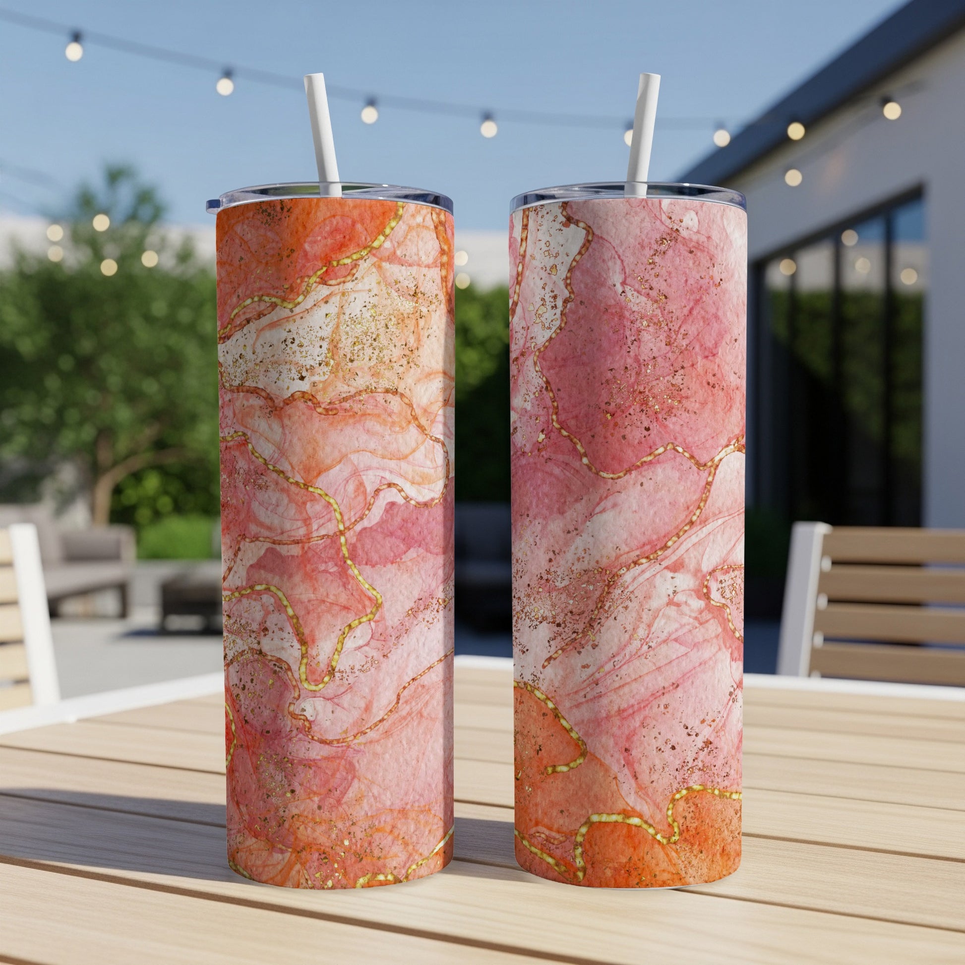 Two tall tumblers with pink and gold marble design on a wooden table.