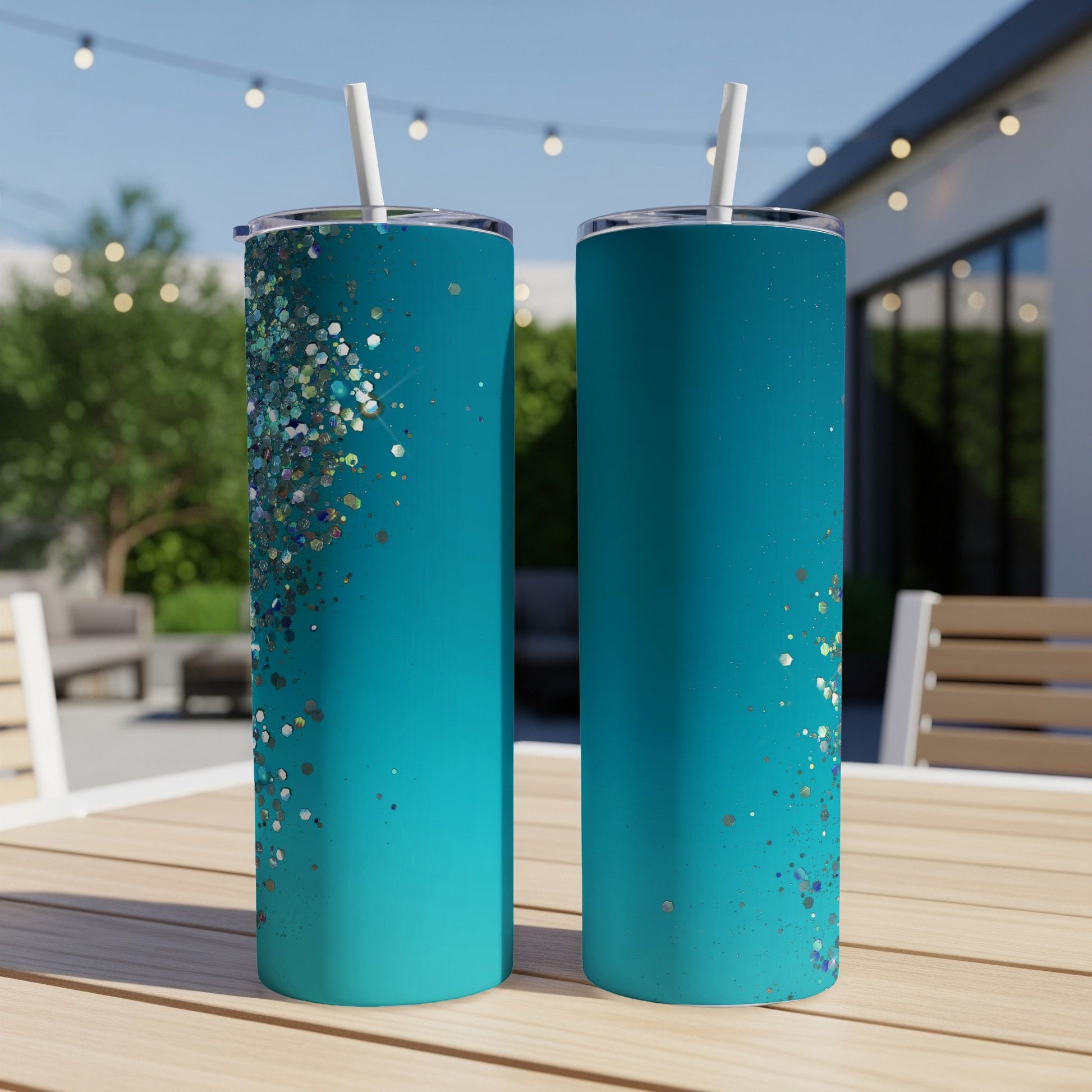 Two teal tumblers with scattered glitter designs and white straws on a wooden table.