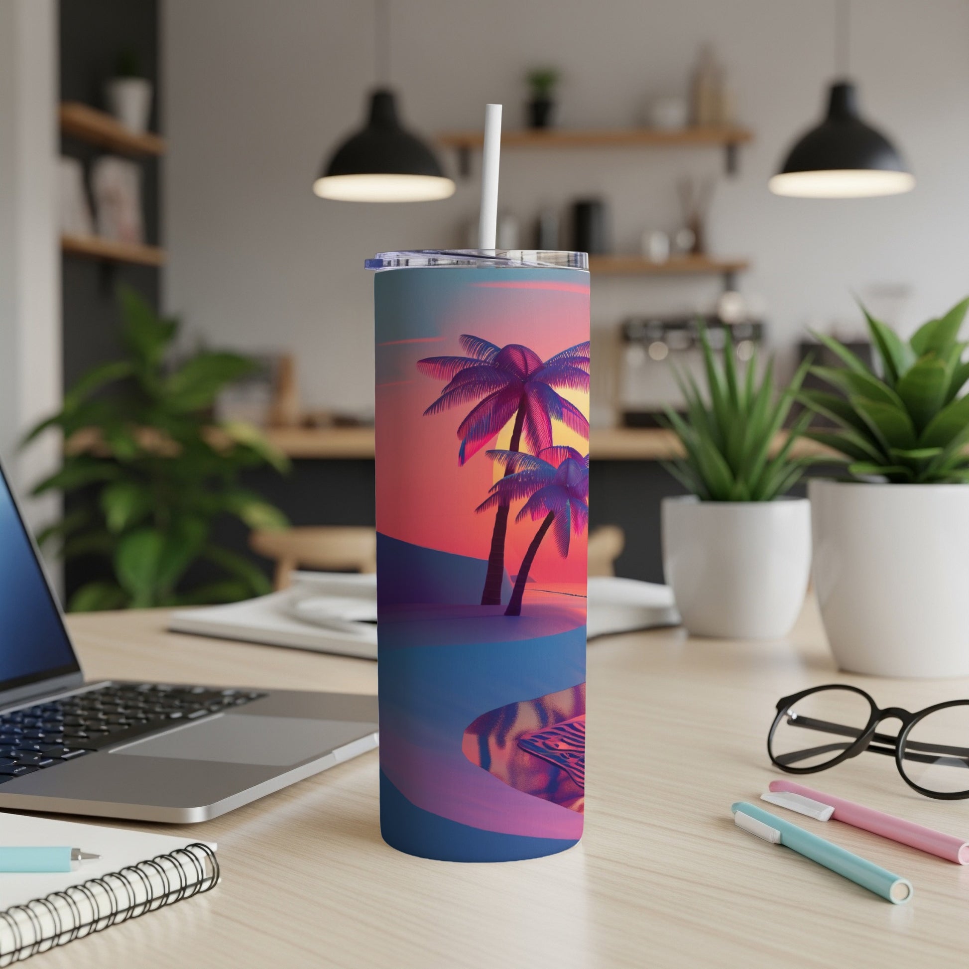 Tumbler with sunset palm trees and pool scene, on a desk with laptop and pens.
