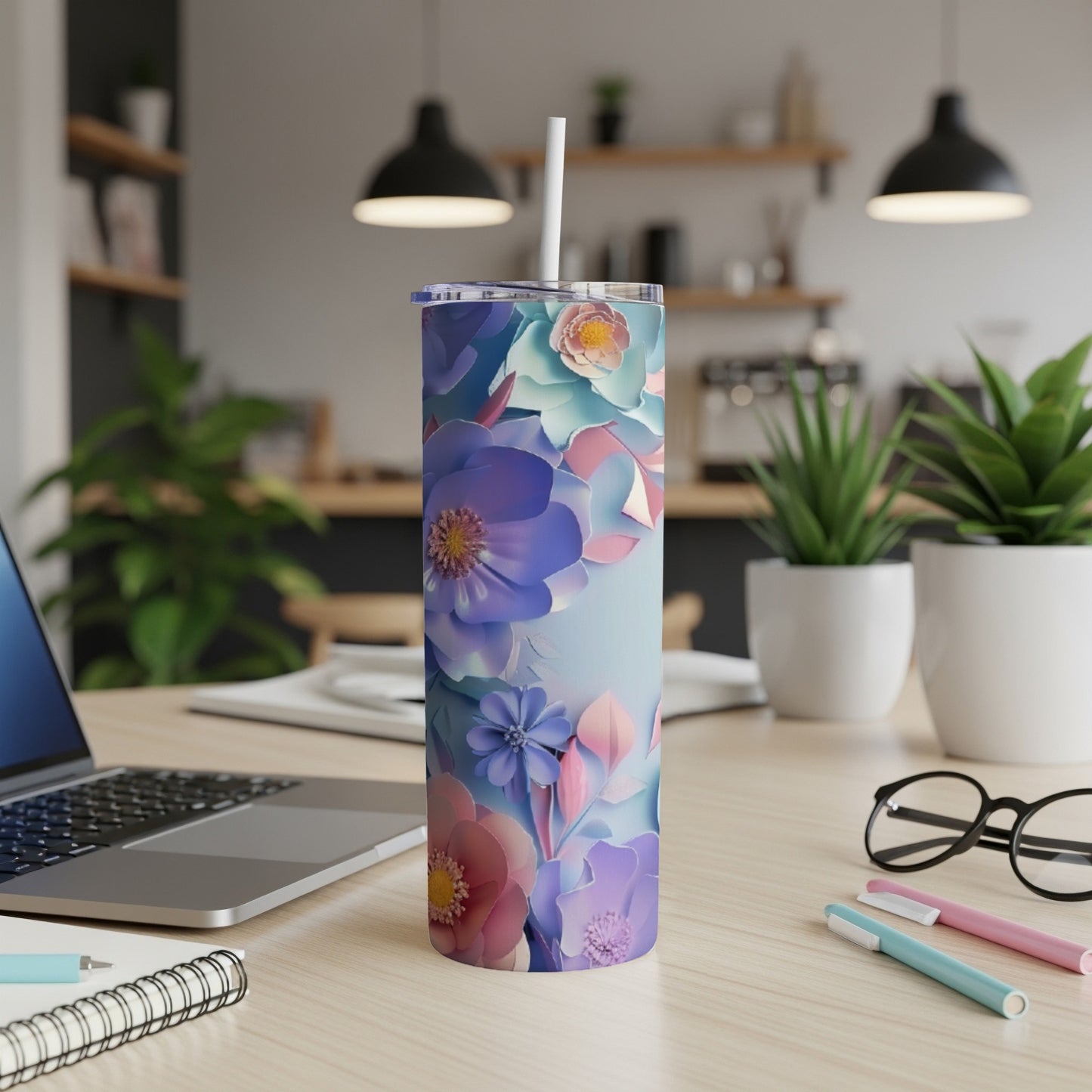 Floral tumbler with straw on a desk with laptop and pens.