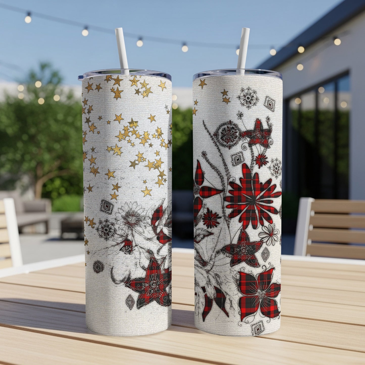 Two floral patterned tumblers with straws on a wooden table outdoors.