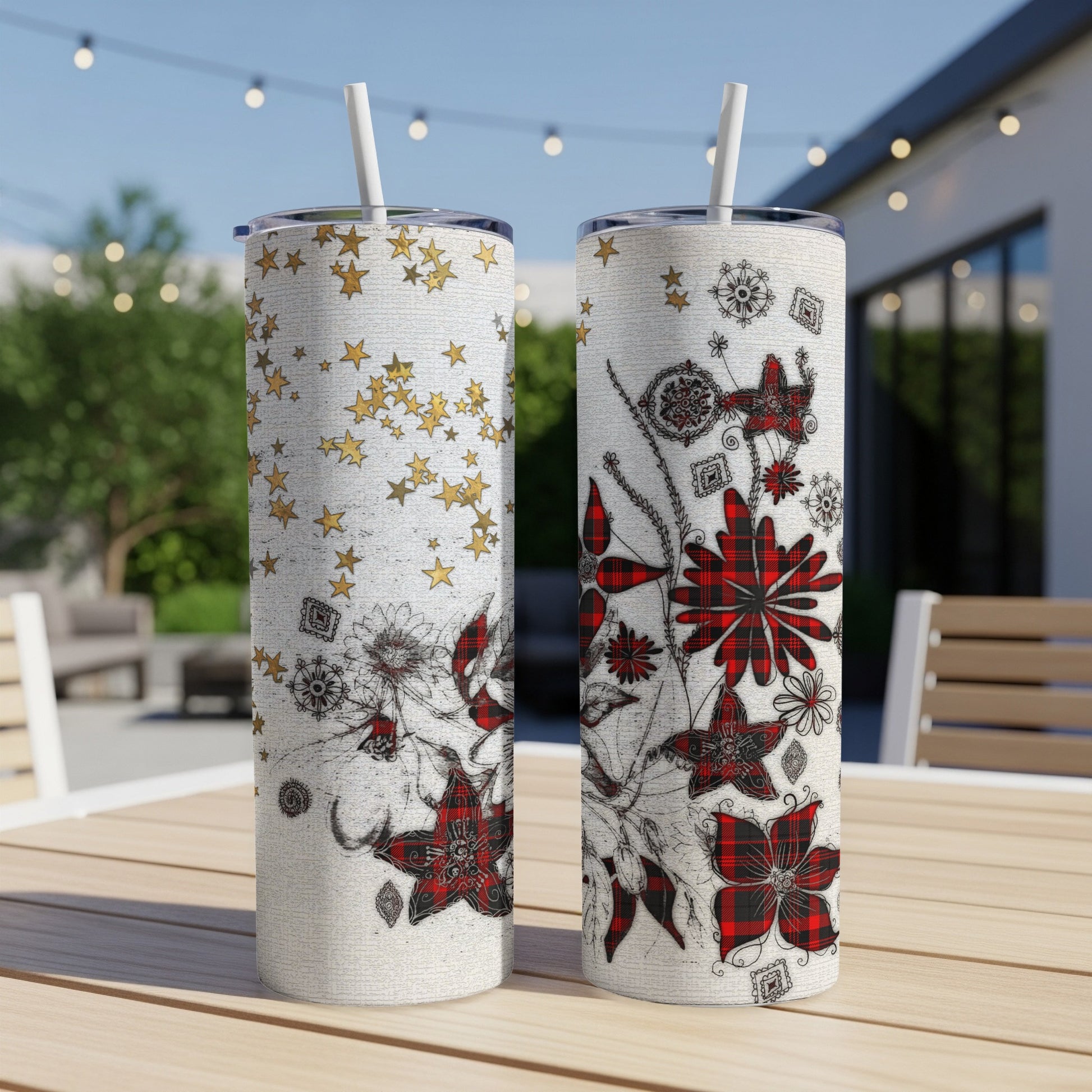 Two floral patterned tumblers with straws on a wooden table outdoors.