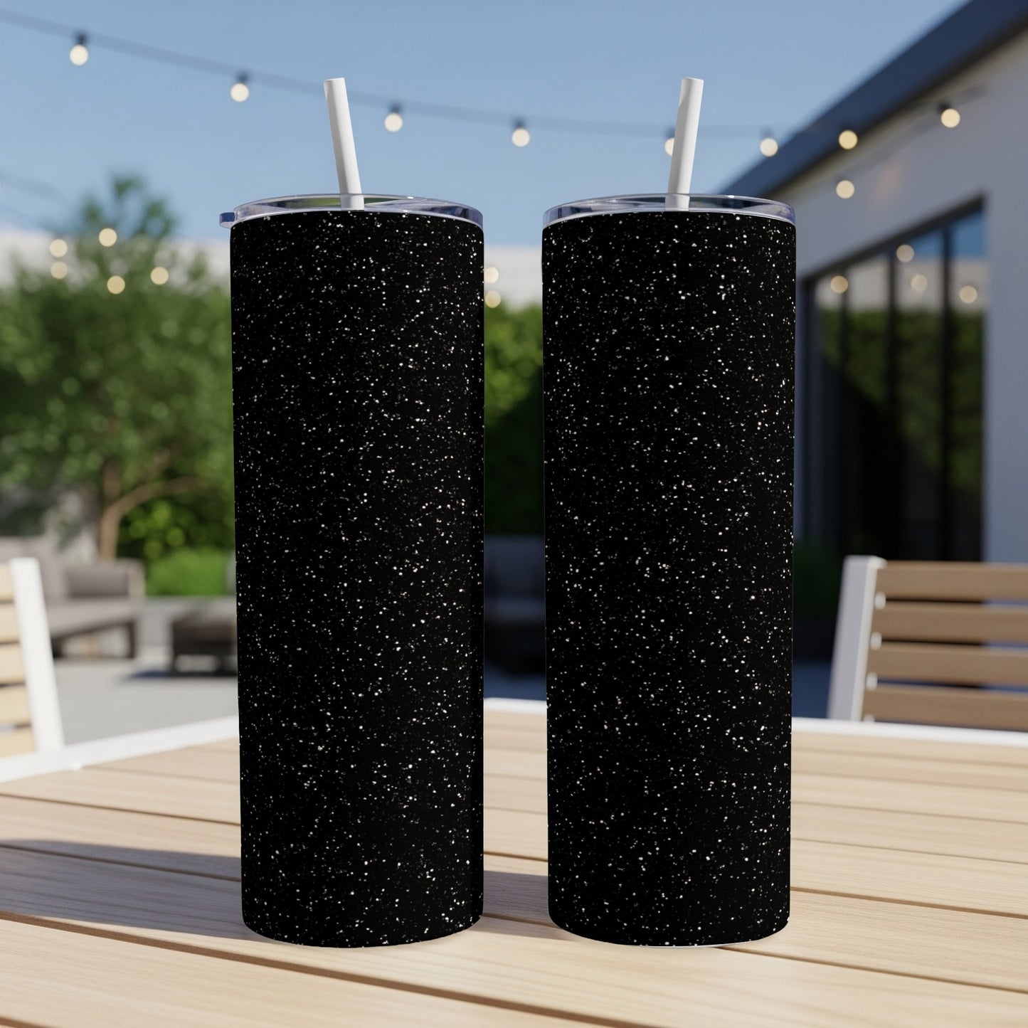 Two black tumblers with a speckled glitter design stand on a wooden table outdoors.