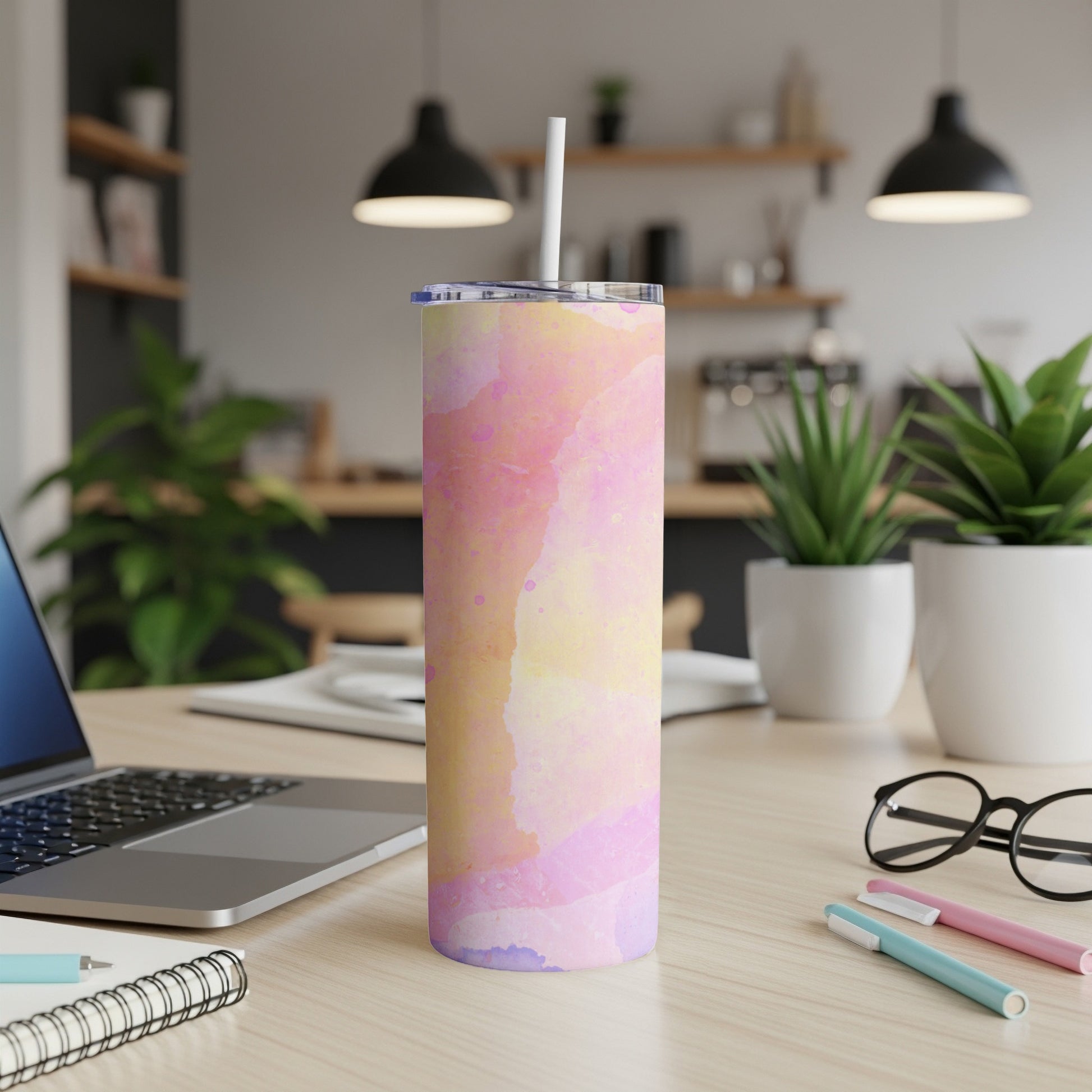 Pink and yellow watercolor patterned tumbler with straw on a desk.