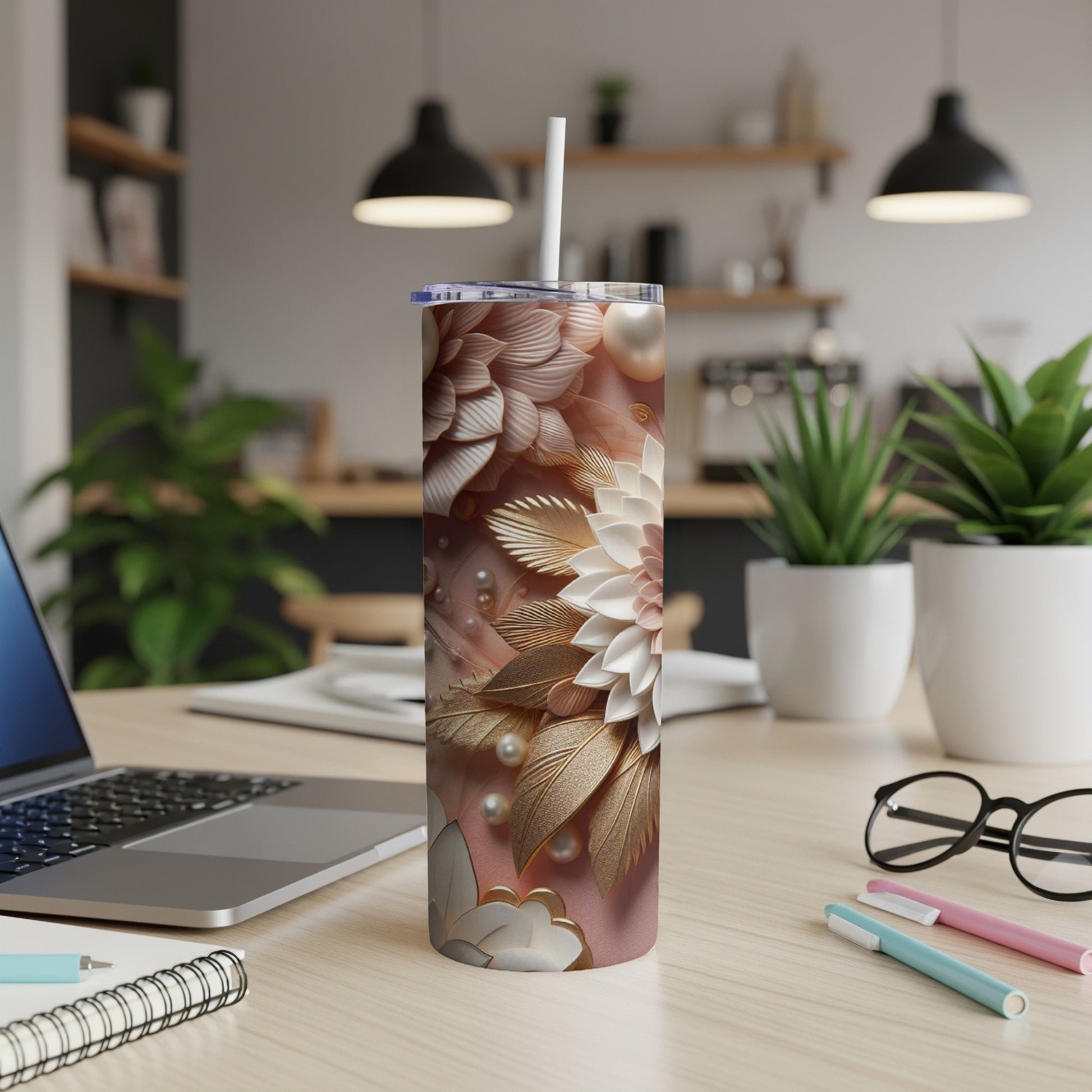 Floral patterned tumbler with straw on a desk, with a laptop and pens.