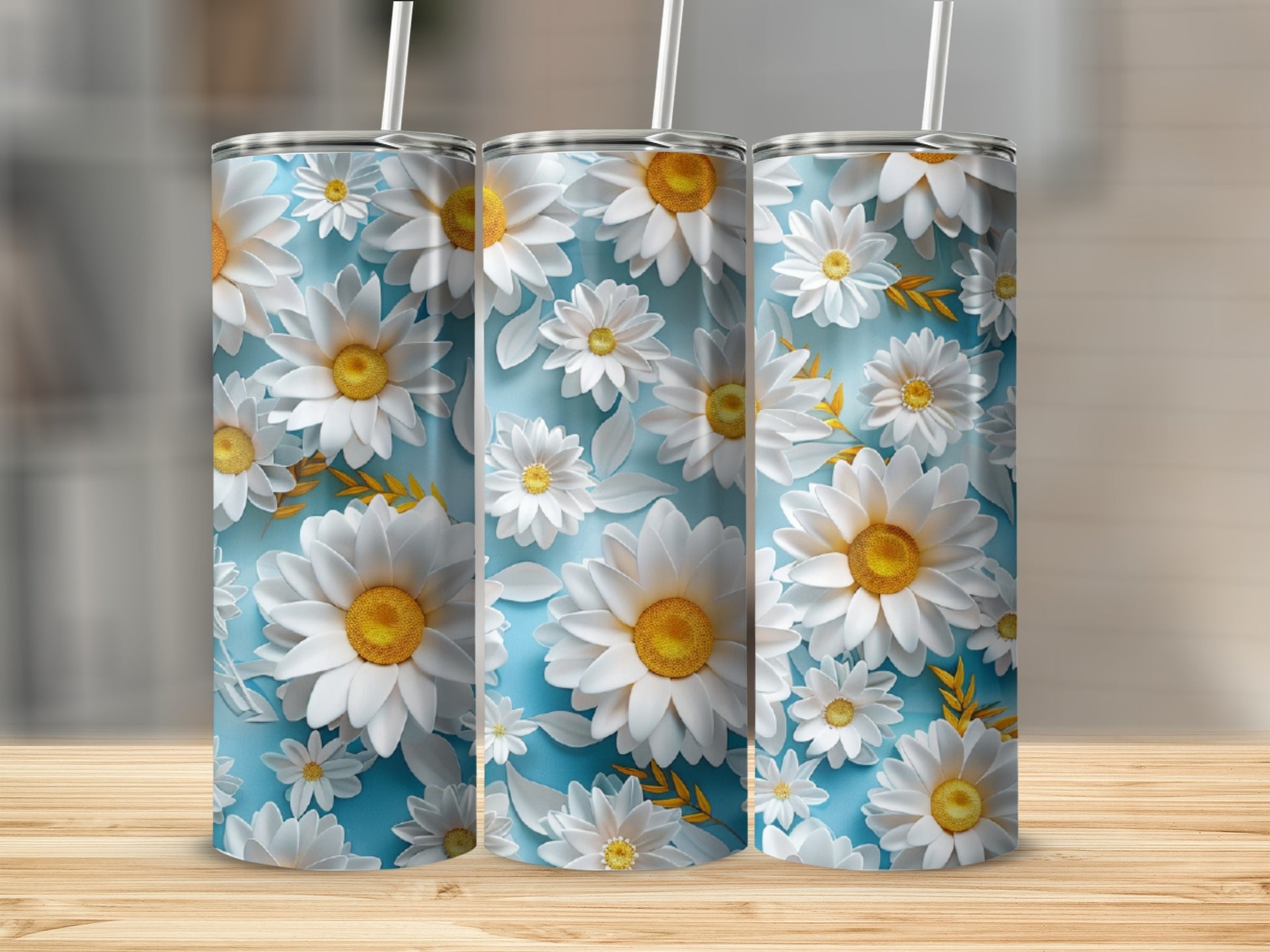 Three tumblers adorned with a pattern of white daisies and green leaves on a blue background.