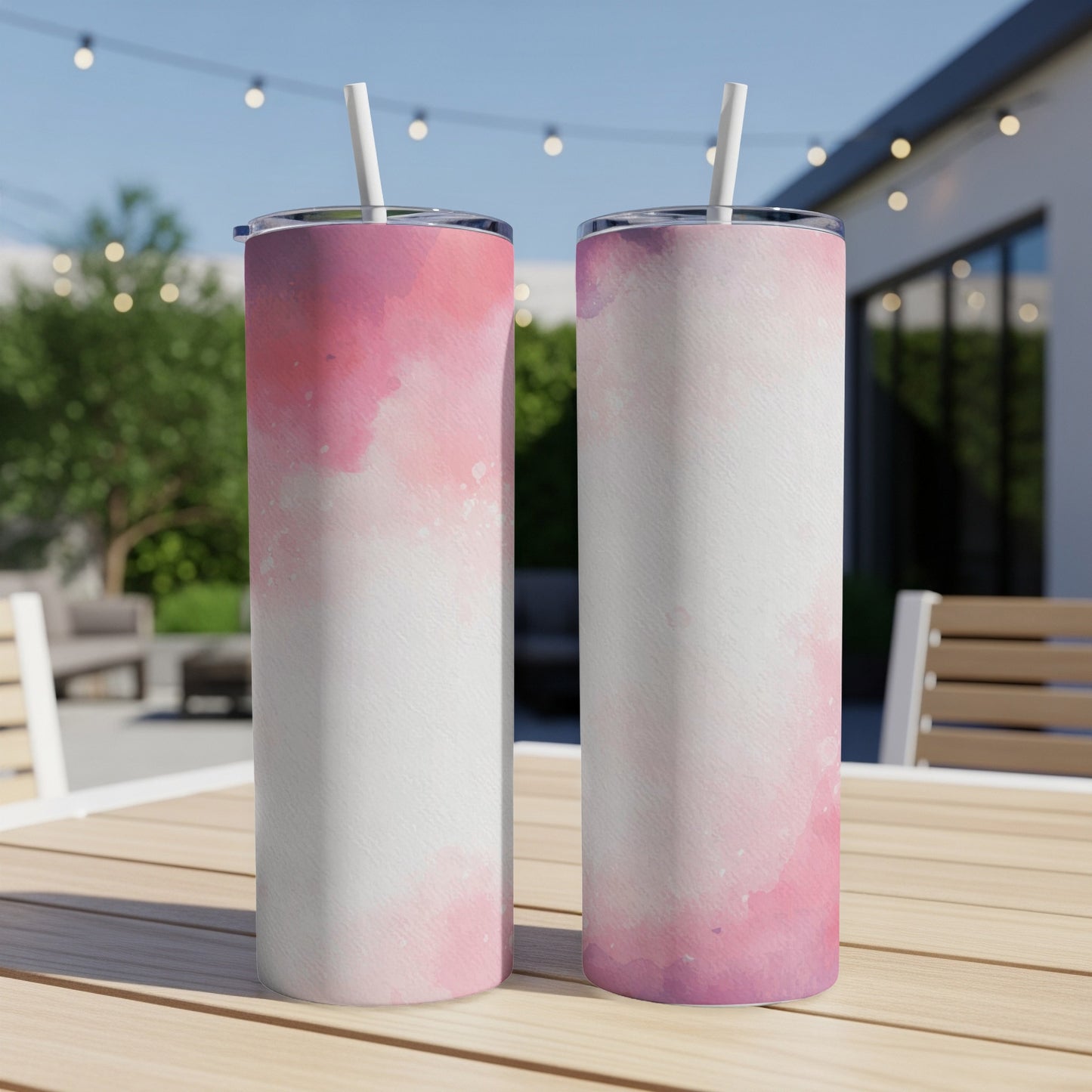 Two tumblers with pink watercolor design stand on a wooden table outdoors.
