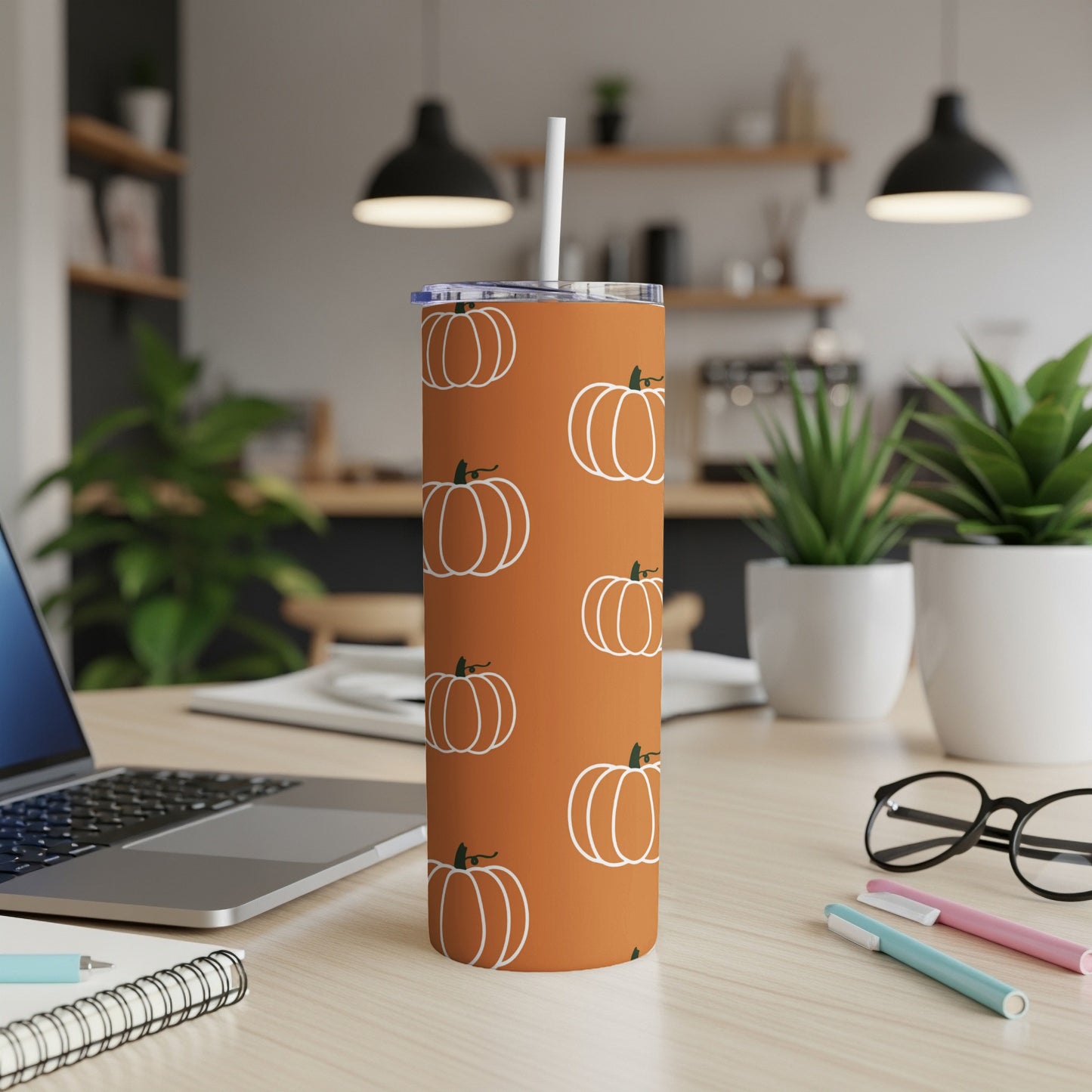 Orange tumbler with white pumpkin pattern and straw on a desk.