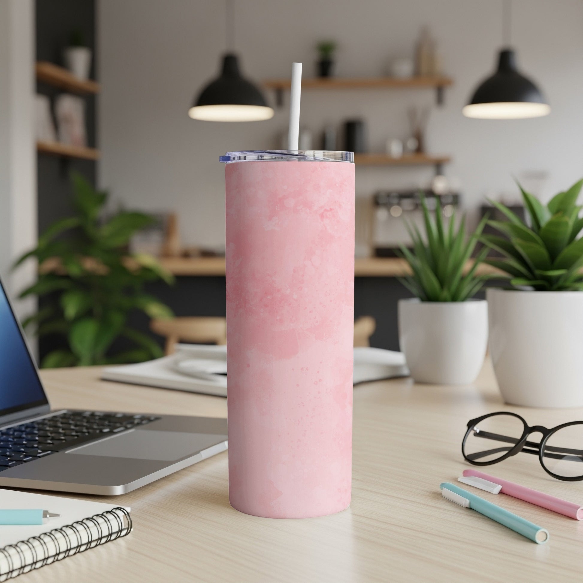 Pink marbled tumbler with straw on a desk with laptop and plants.