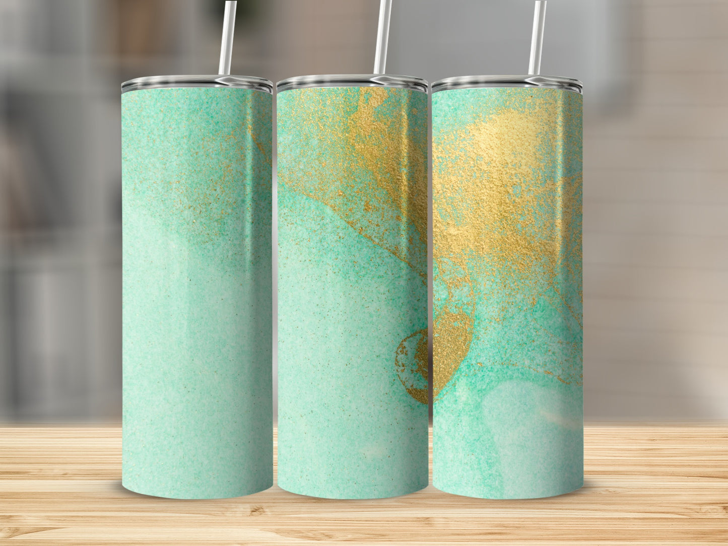 Three tumblers with a watercolor and gold splatter design on a wooden surface.
