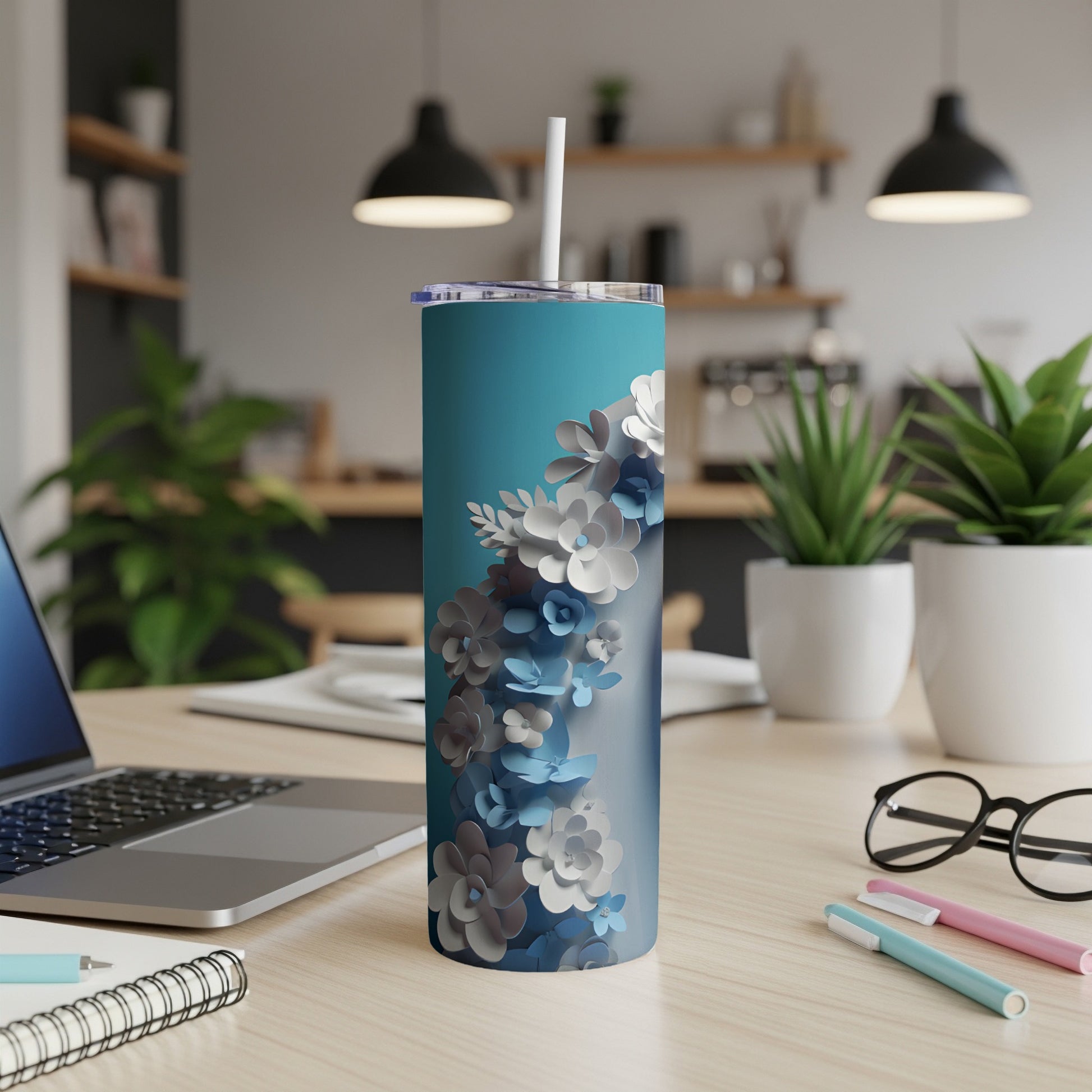 Turquoise tumbler with floral pattern, on a desk with laptop and pens.