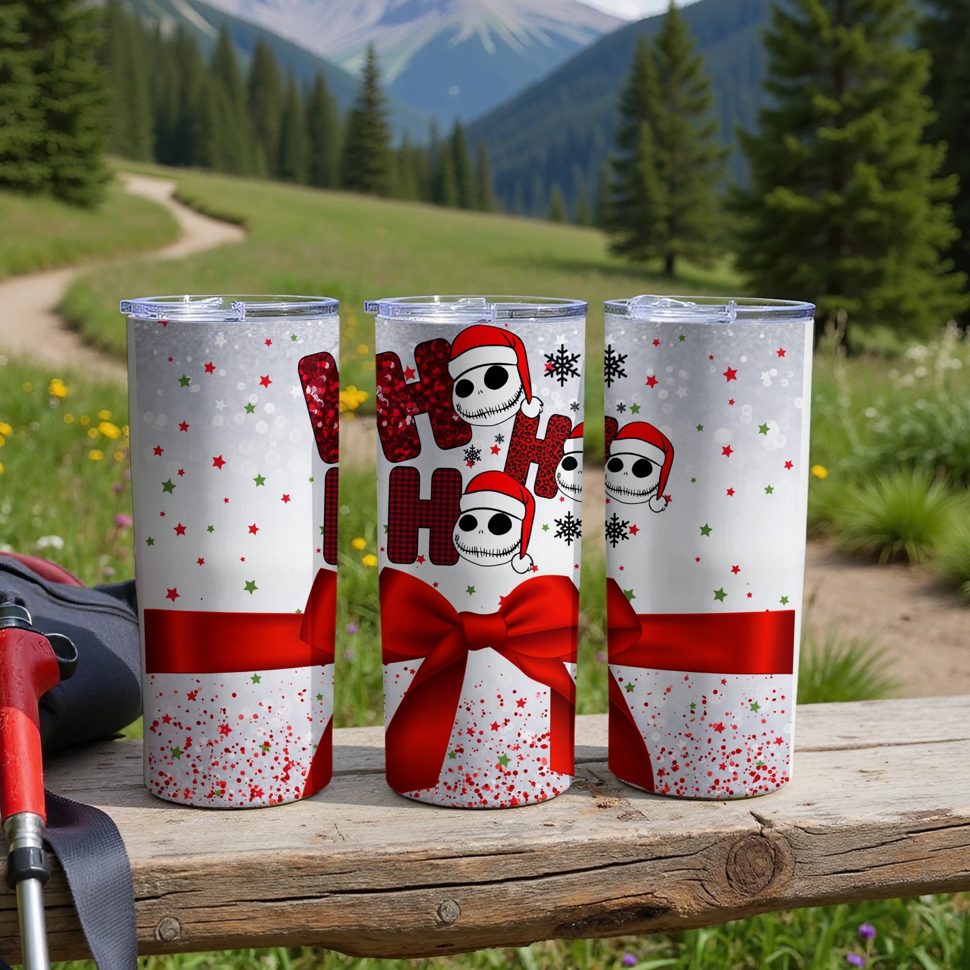 Three Santa hat wearing Jack Skellington tumblers with red bows on a wooden surface.