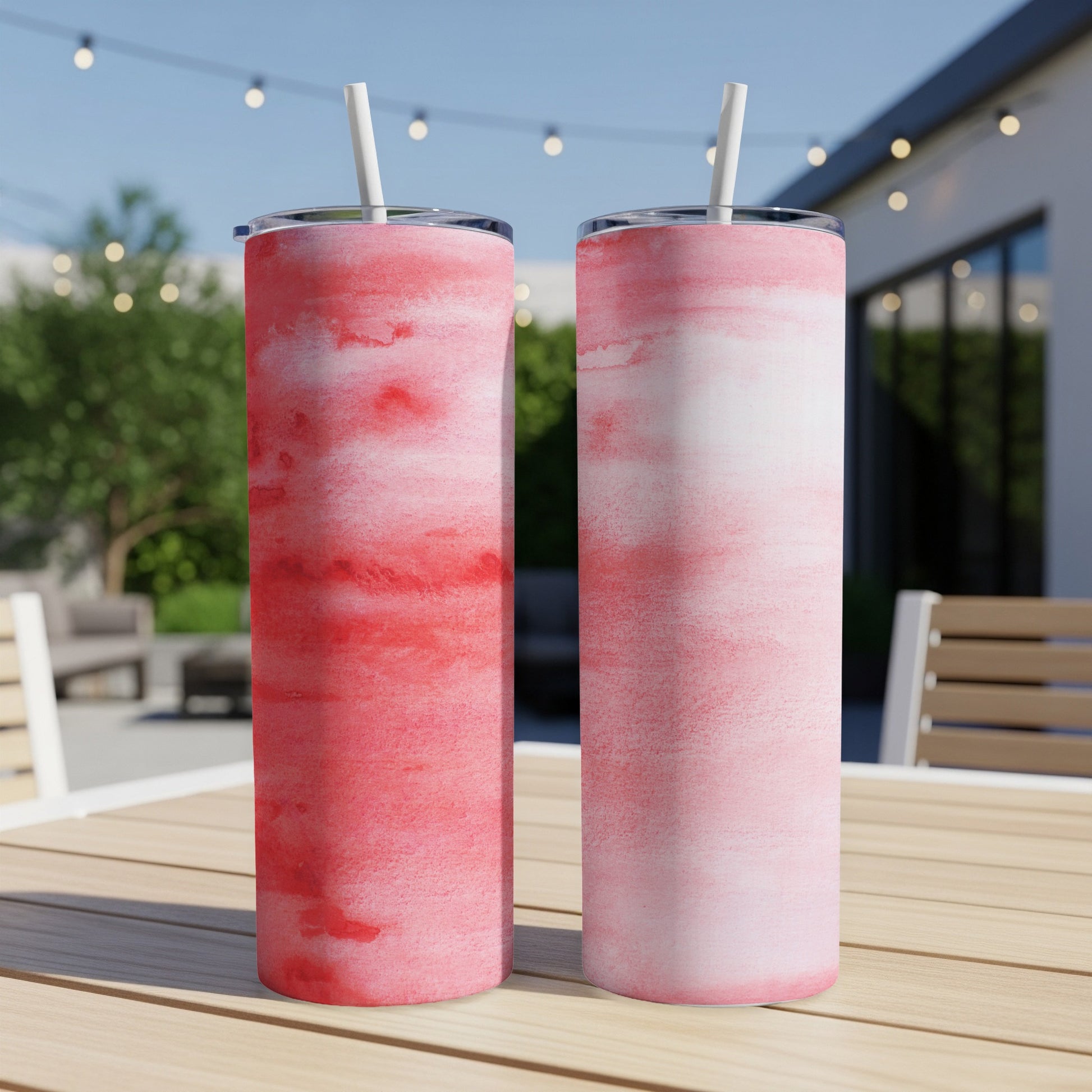 Two tumblers with a pink watercolor design and straws on a wooden table.