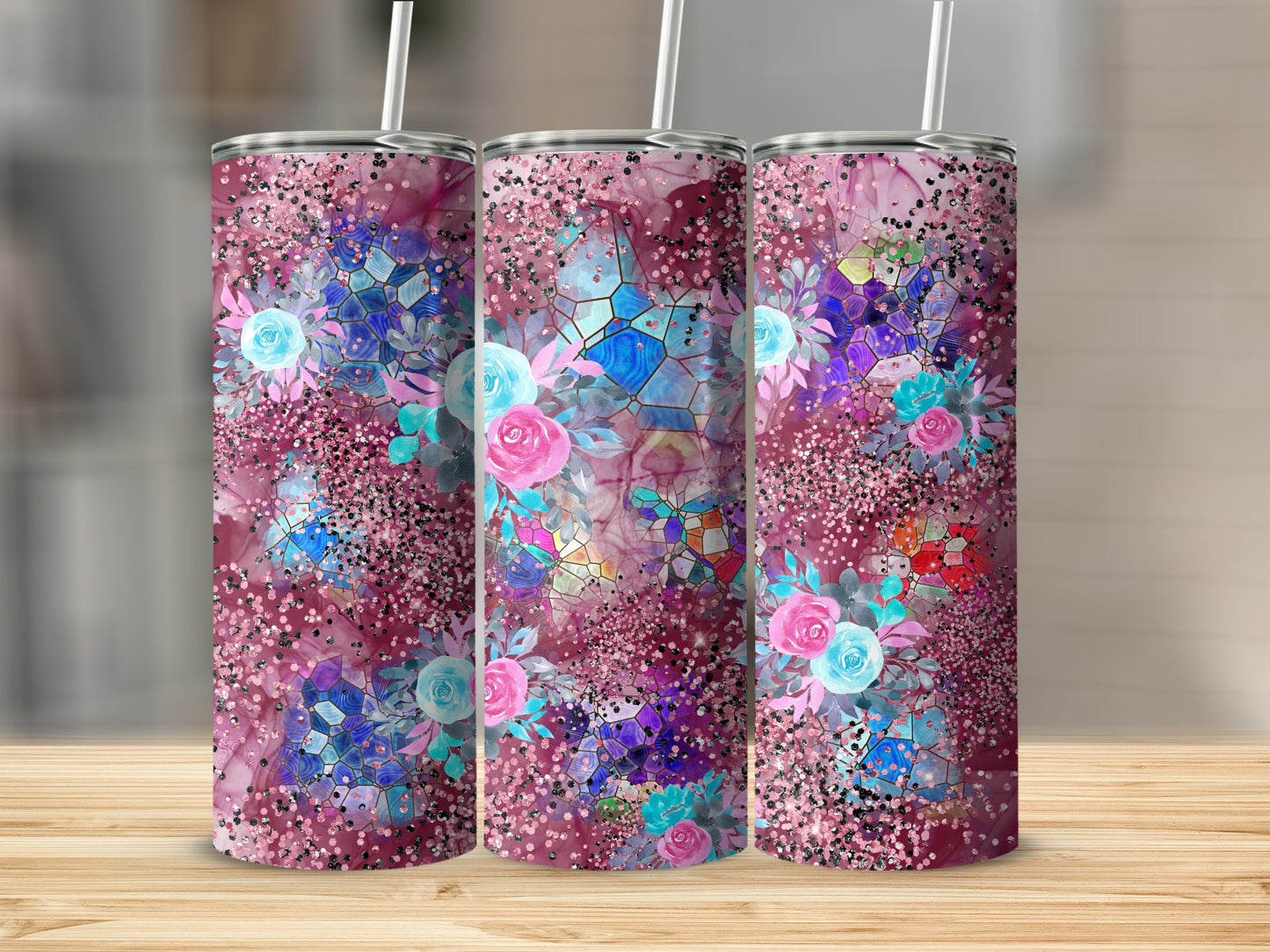 Three tall tumblers with floral and glitter designs on a wooden surface.