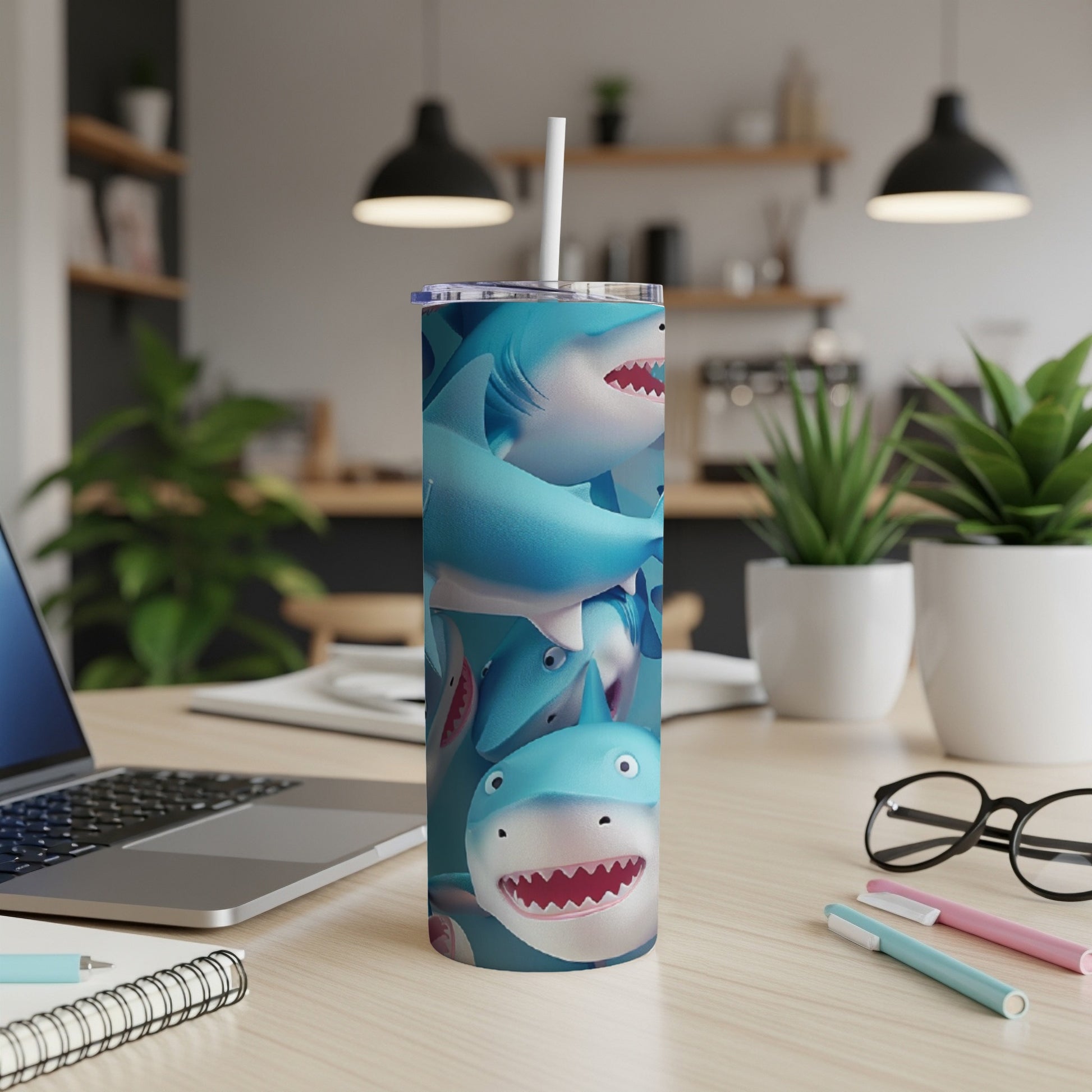 Blue cartoon sharks on a white tumbler with a straw, on a desk.