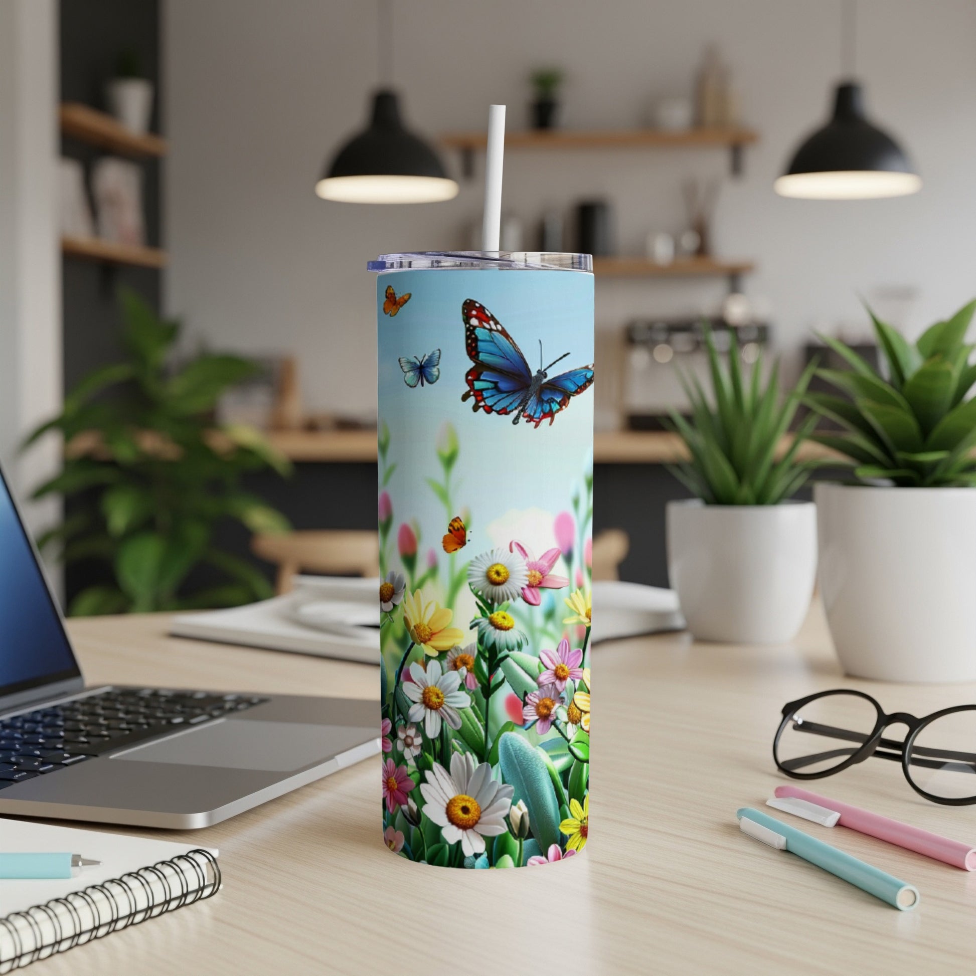 Tumbler with butterflies and colorful flowers, on a desk with laptop.