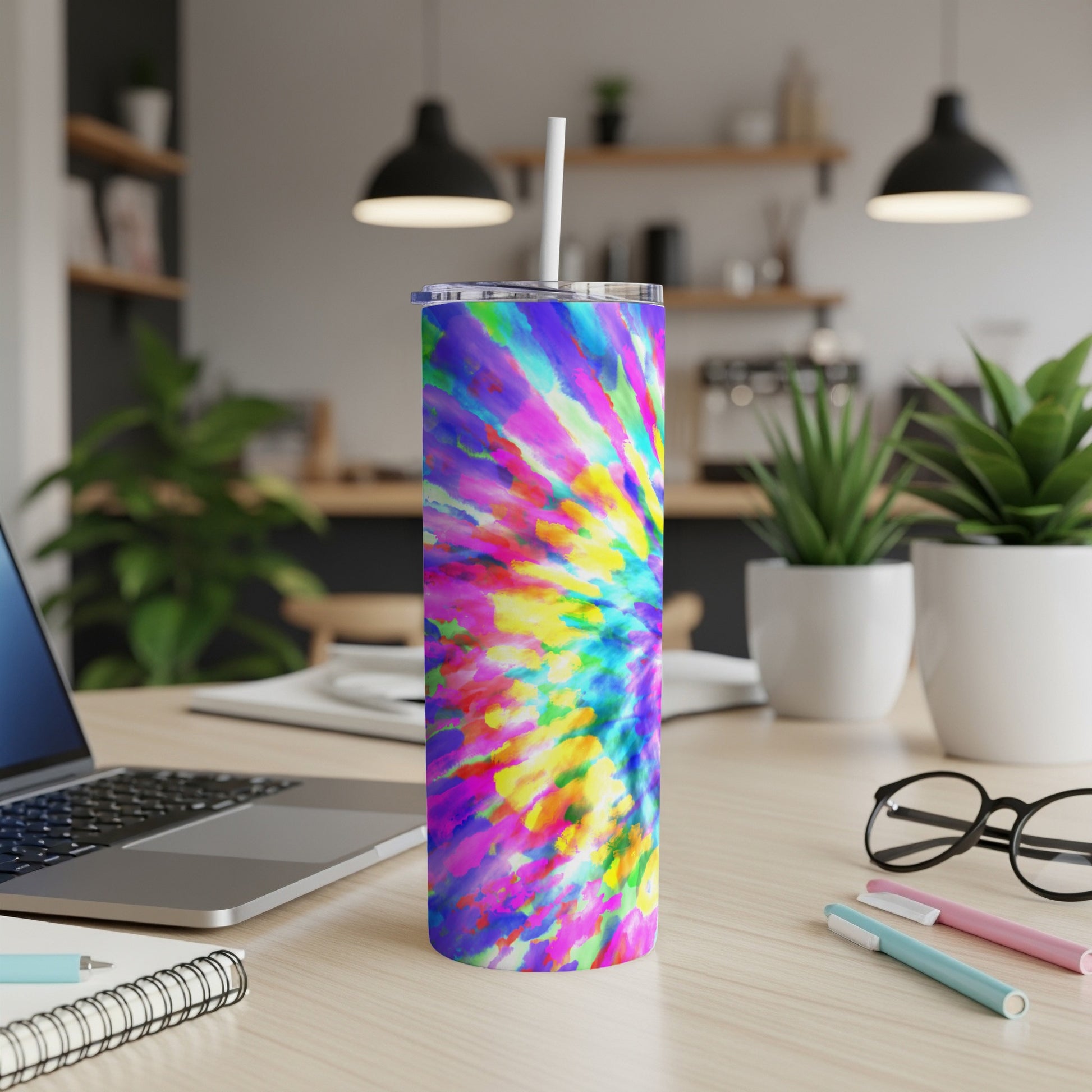 Colorful tie-dye tumbler with straw on a desk next to a laptop.