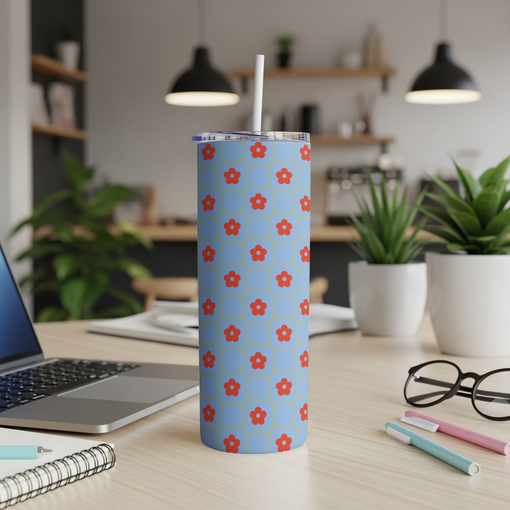 Blue tumbler with red floral pattern and white straw on a desk.
