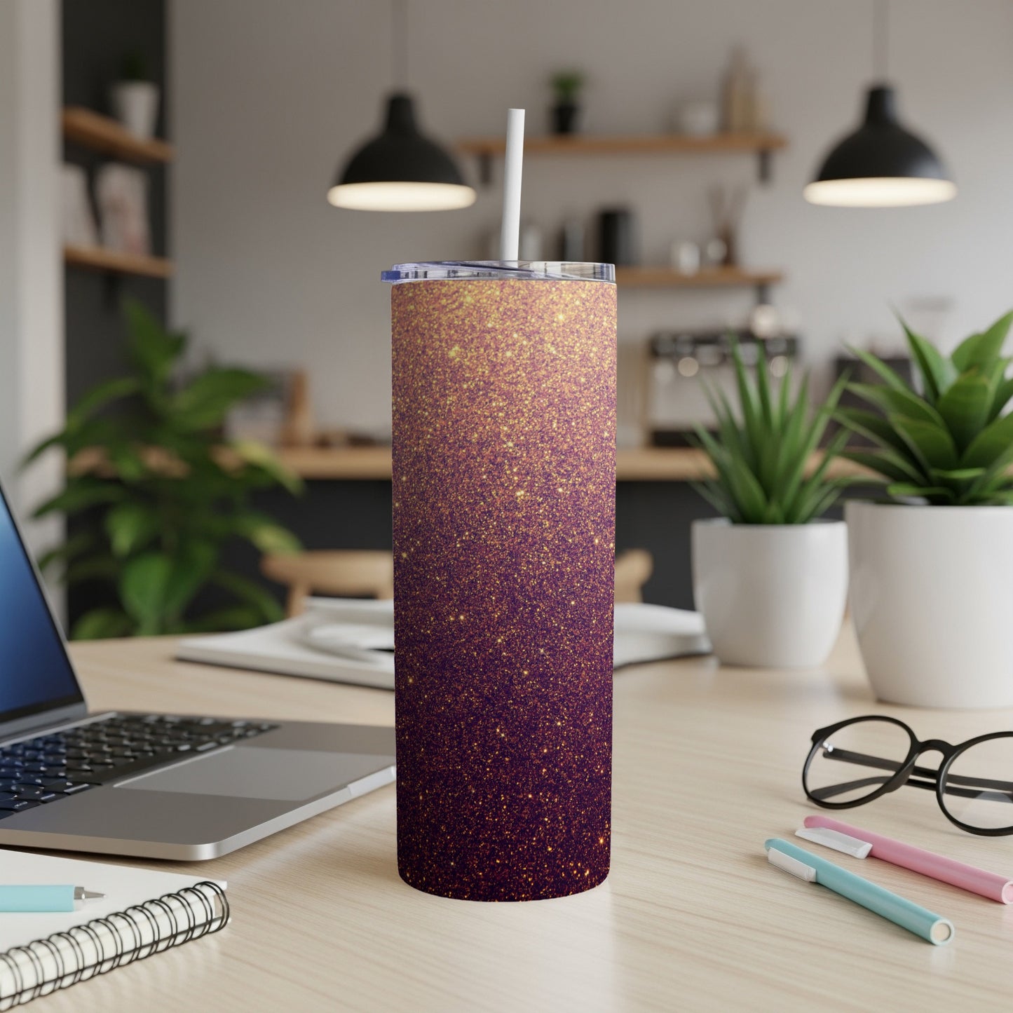 Purple and gold glitter tumbler with straw on a desk.