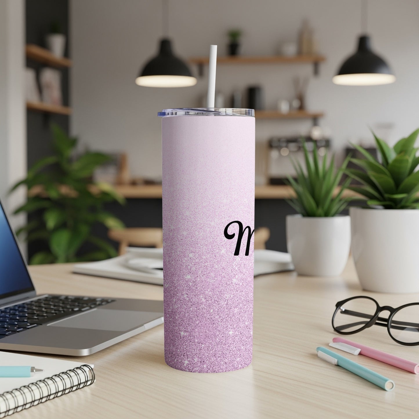 Pink glitter tumbler with a black initial M on a desk.