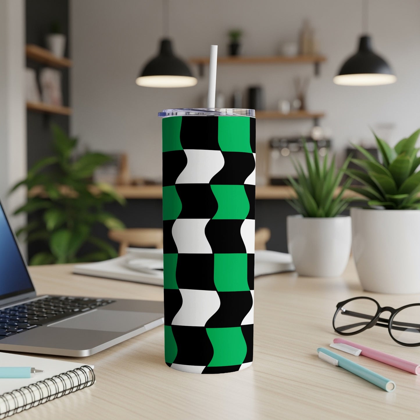 Green and black checkerboard pattern tumbler with white straw on a desk.