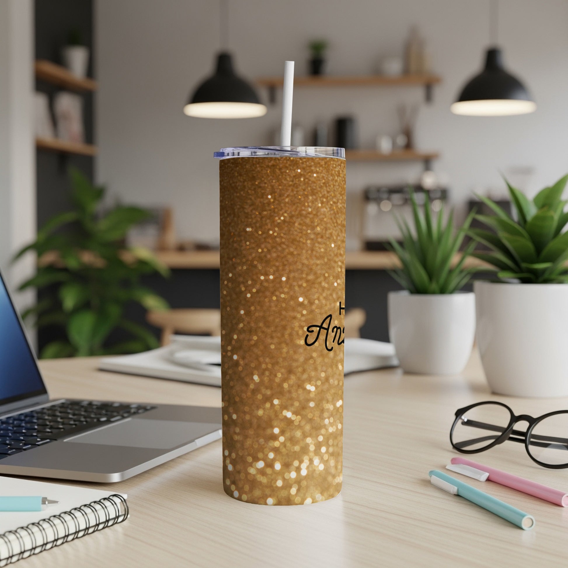 Gold glitter tumbler with "Happy Anniversary" text and straw on a desk.