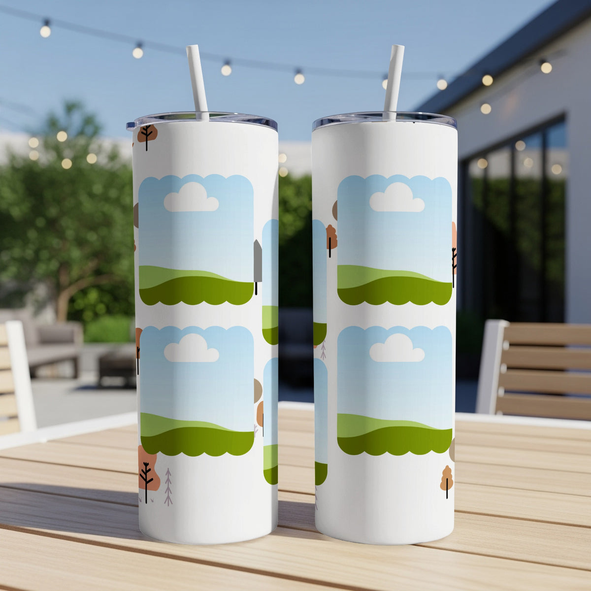 Two white tumblers with a cartoon landscape design, outdoors on a table.