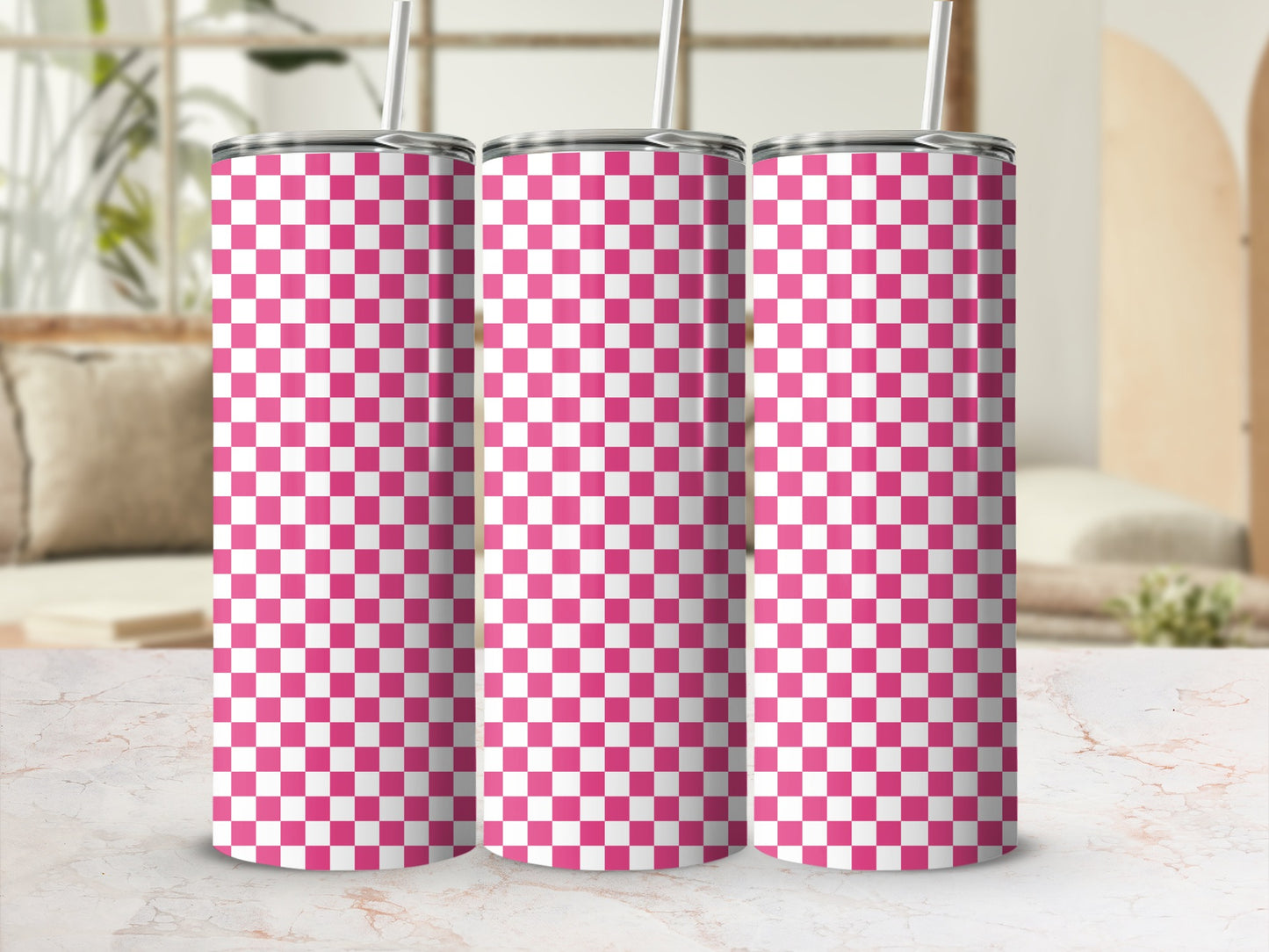 Three pink and white checkered tumblers with straws stand on a marble surface.