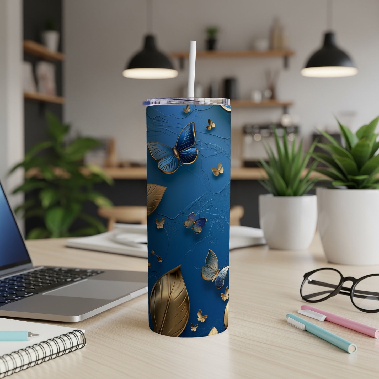 Blue tumbler with gold butterflies and leaves, on a desk.