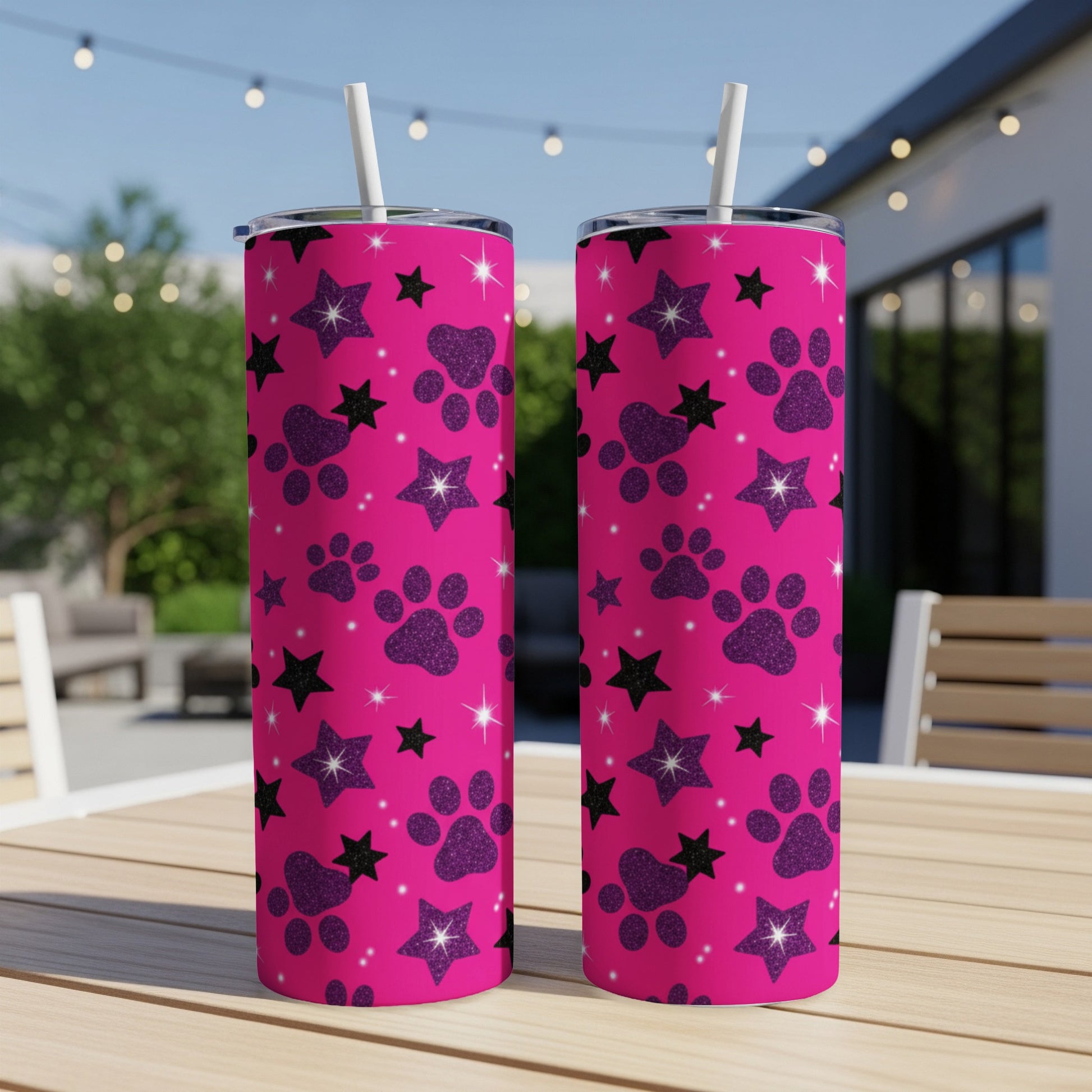 Two pink tumblers with paw prints and stars pattern, on an outdoor table.