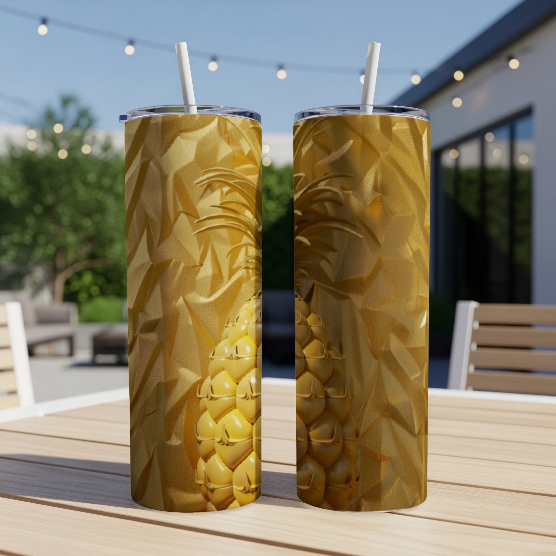 Two gold pineapple tumblers with straws on a table.